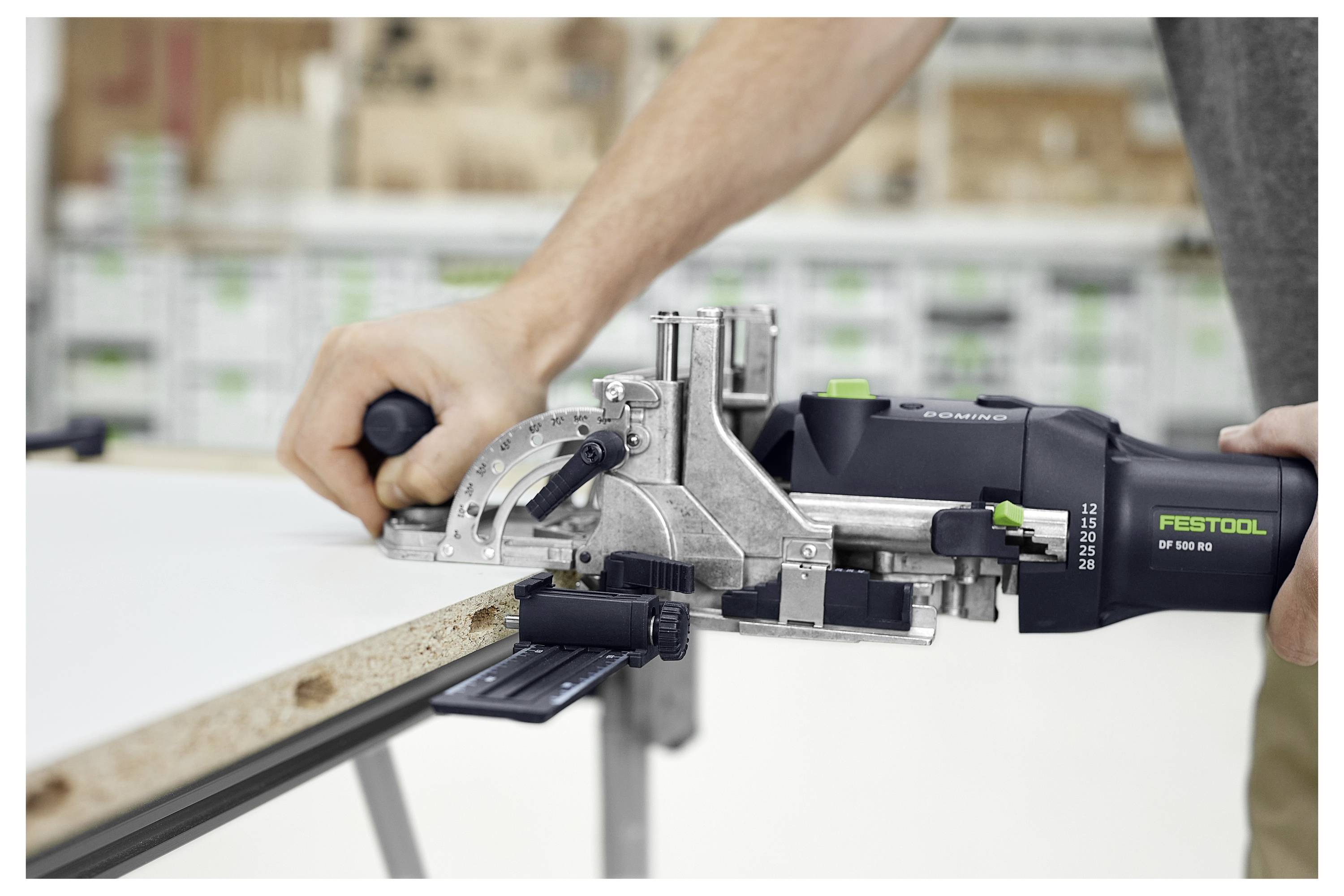 Ein Mann mit Schutzbrille benutzt einen Elektroschleiffer an einem Holztisch in einer Werkstatt. Er konzentriert sich darauf, die Oberfläche zu glätten.