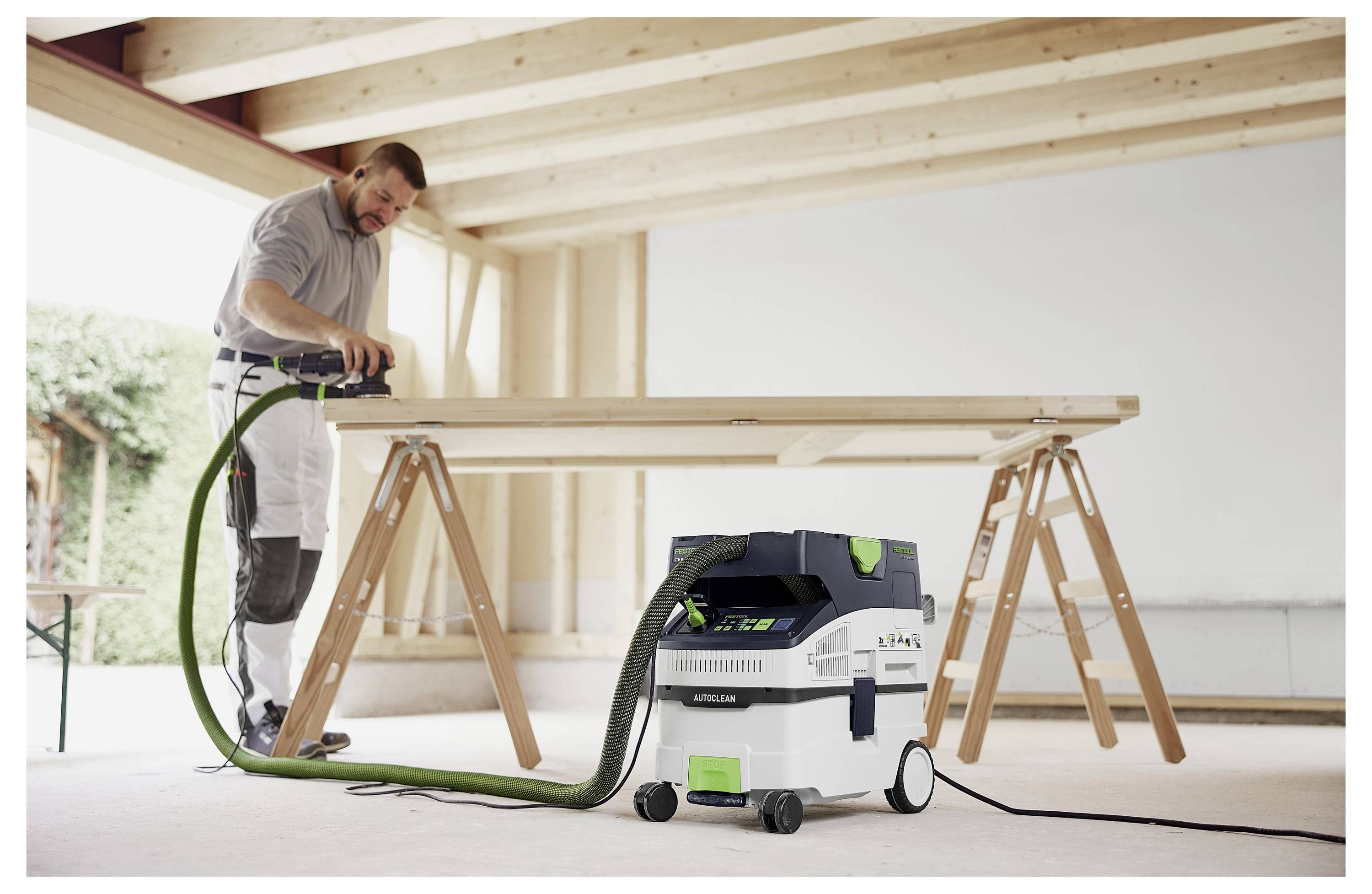 Ein Mann schleifen Holz auf einem Tisch in einer Werkstatt, mit einem Staubsaugsystem angeschlossen, um Staub zu minimieren.