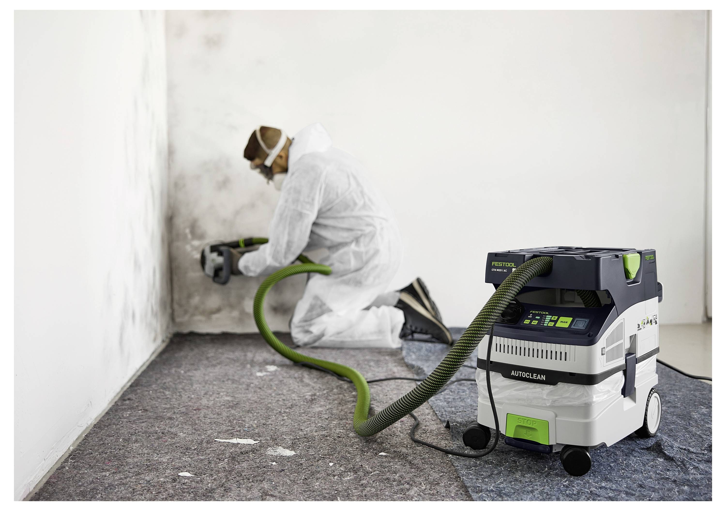 Eine Person in Schutzausrüstung reinigt Schimmel an einer Wand mit einem Staubsaugersystem und unterstreicht dabei die Sicherheit bei der Schimmelentfernung oder Reinigung.