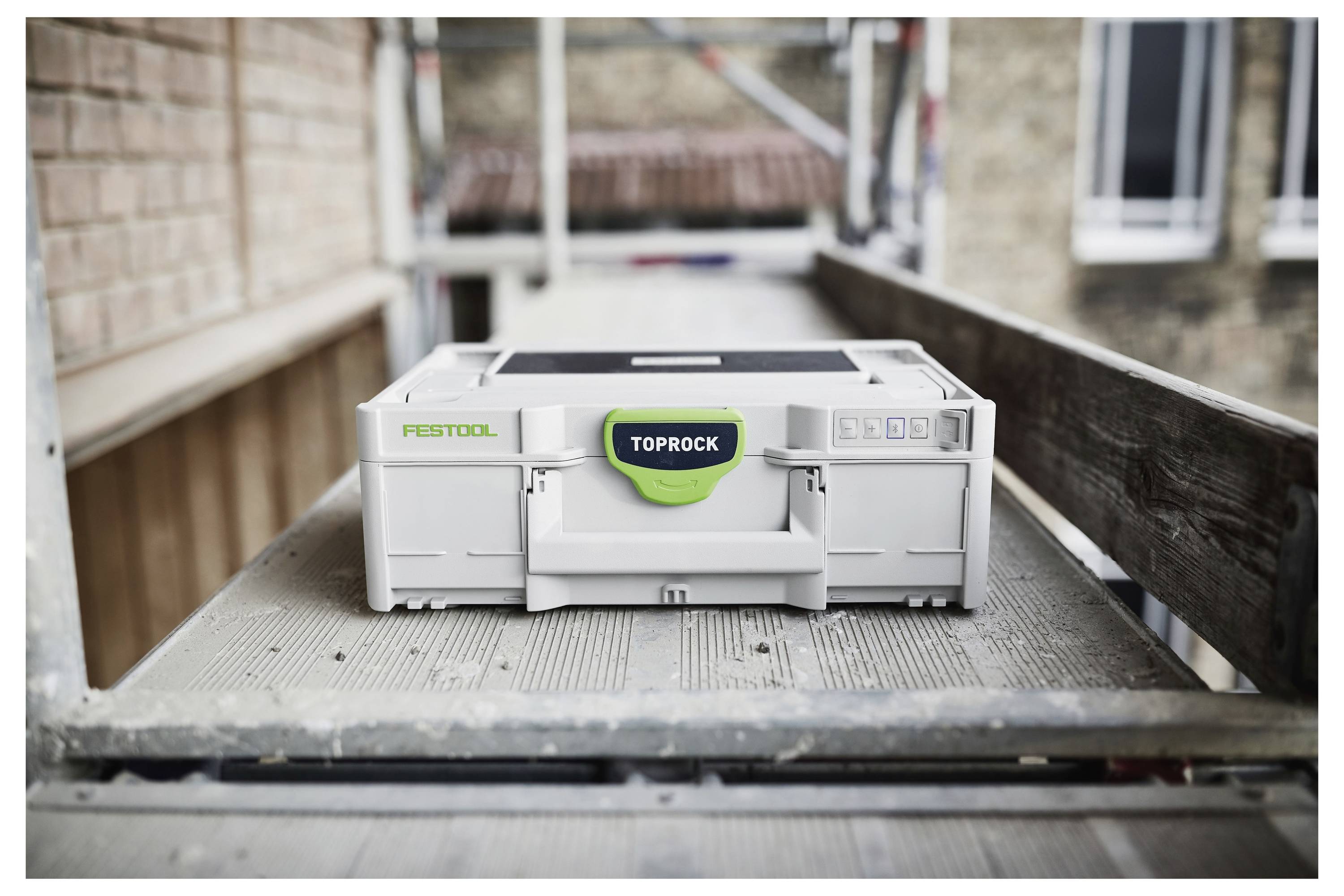 Eine Person mit Schutzbrille verwendet einen Elektroschleiffer mit langem Griff, um eine Wand in einem Baubereich zu glätten.