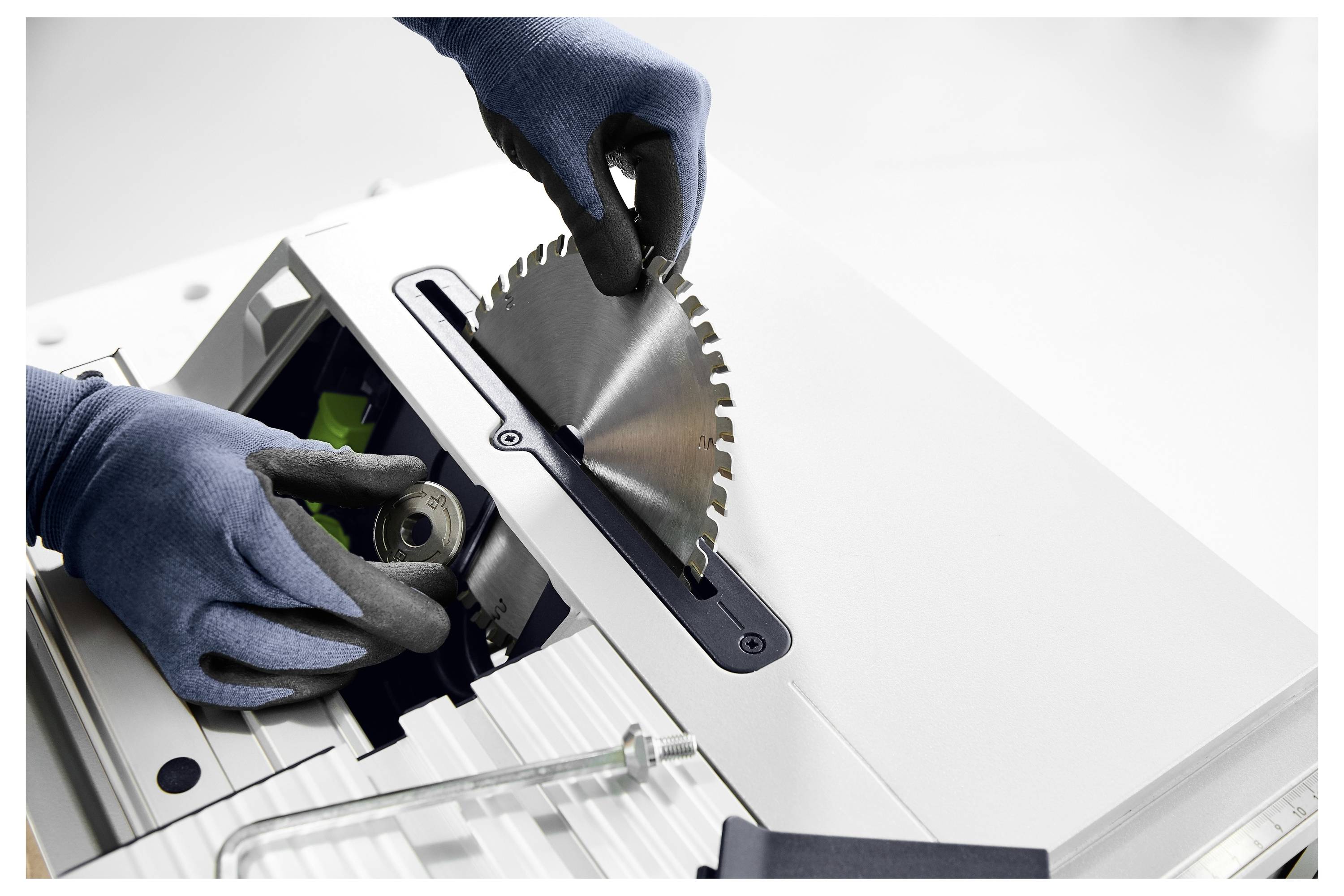 Zwei behandschuhte Hände installieren ein kreisförmiges Sägeblatt in eine Tischkreissäge, was sichere Verfahren zur Geräteinstallation veranschaulicht.