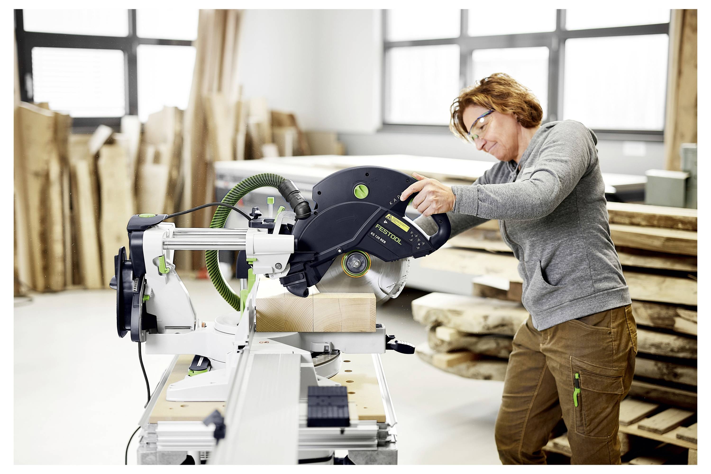 Eine Person, die in einer Werkstatt mit einer Kreissäge Holz schneidet, umgeben von Holzbrettern und Werkzeugen, konzentriert auf präzise Arbeit.