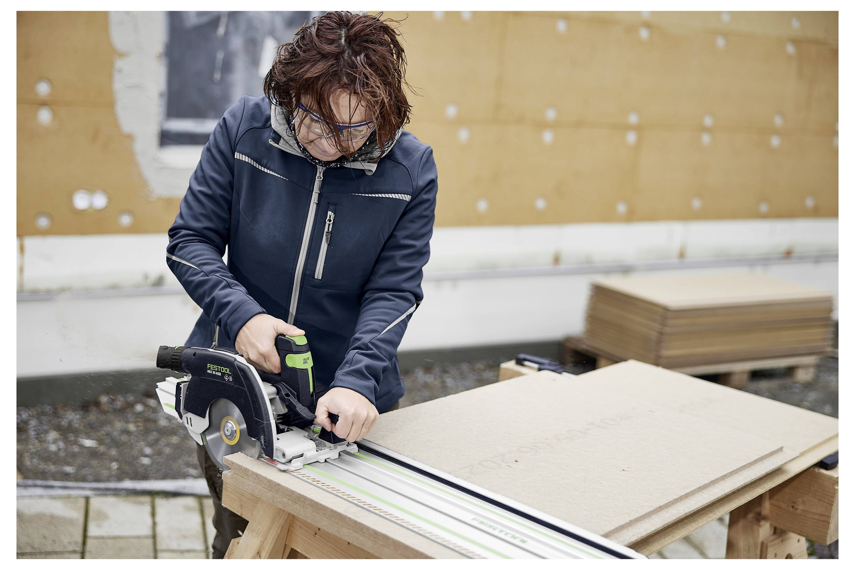 Eine weiße Festool-Werkzeugkiste mit mehreren Schubladen und grünen Griffen, dargestellt auf einer Werkbank in einer Werkstattsituation.