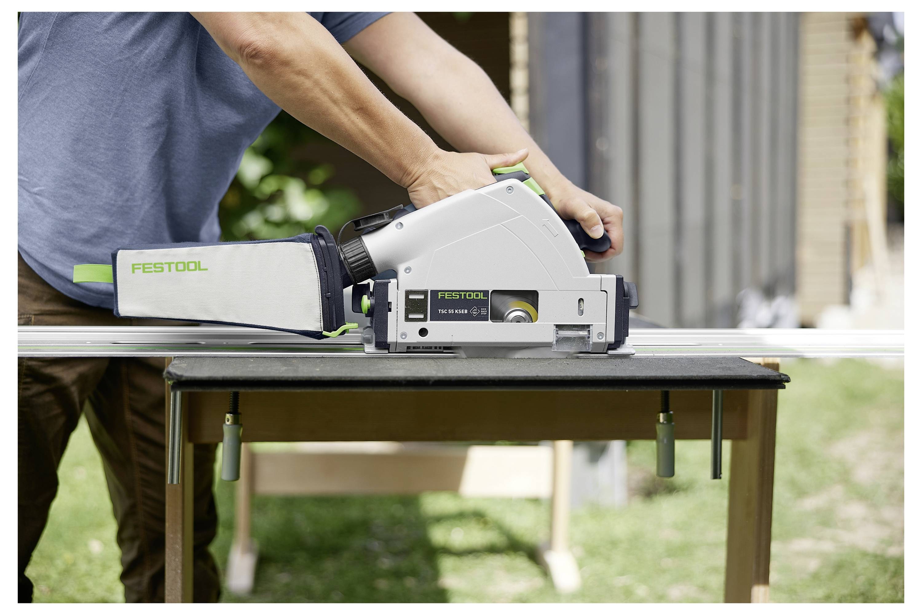A person using a Festool track saw on a workbench for precise cutting of a wooden board in an outdoor setting.
