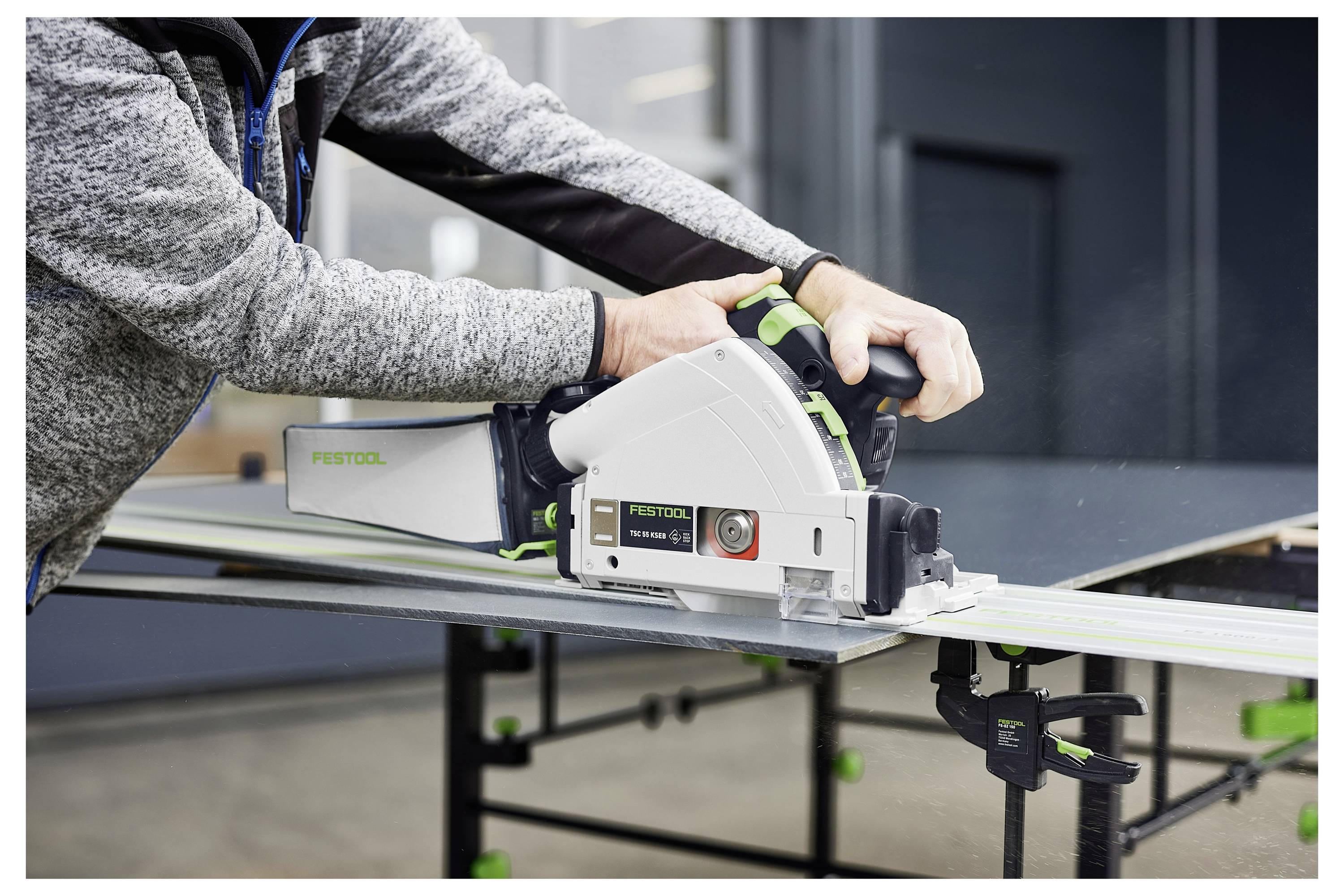 Eine Person verwendet eine Festool-Tauchsäge, um ein Materialblatt auf einer Werkbank zu schneiden, wobei Holzbearbeitungs- oder Bauwerkzeuge in Gebrauch gezeigt werden.