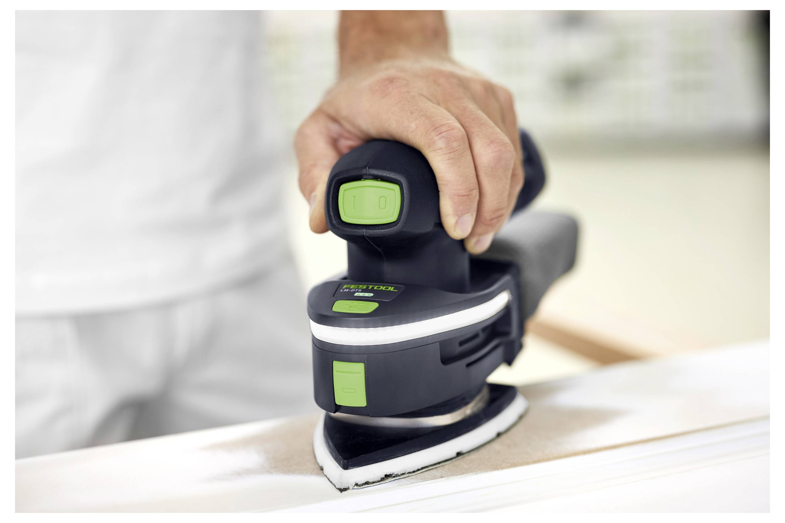 Eine Person benutzt einen tragbaren elektrischen Schleiferauff einer Holzoberfläche und konzentriert sich darauf, die Kanten glatt zu schleifen in einer gut beleuchteten Werkstattumgebung.