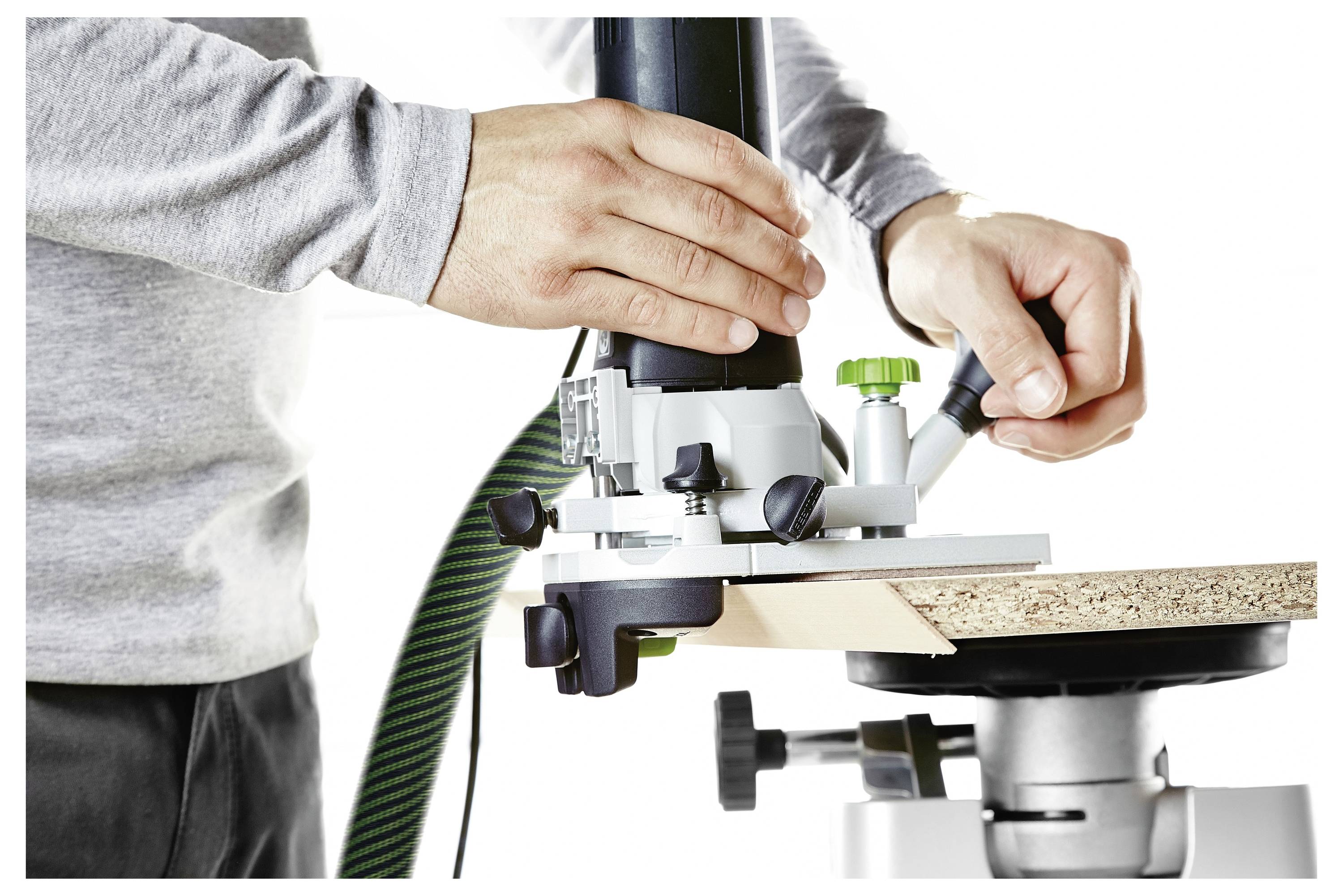 Eine Person benutzt einen Schleifers an einer weißen Wand in einem Zimmer. Ein Staubsauger und Werkzeuge liegen auf dem Boden, mit einem leichten Stativ in der Nähe positioniert.