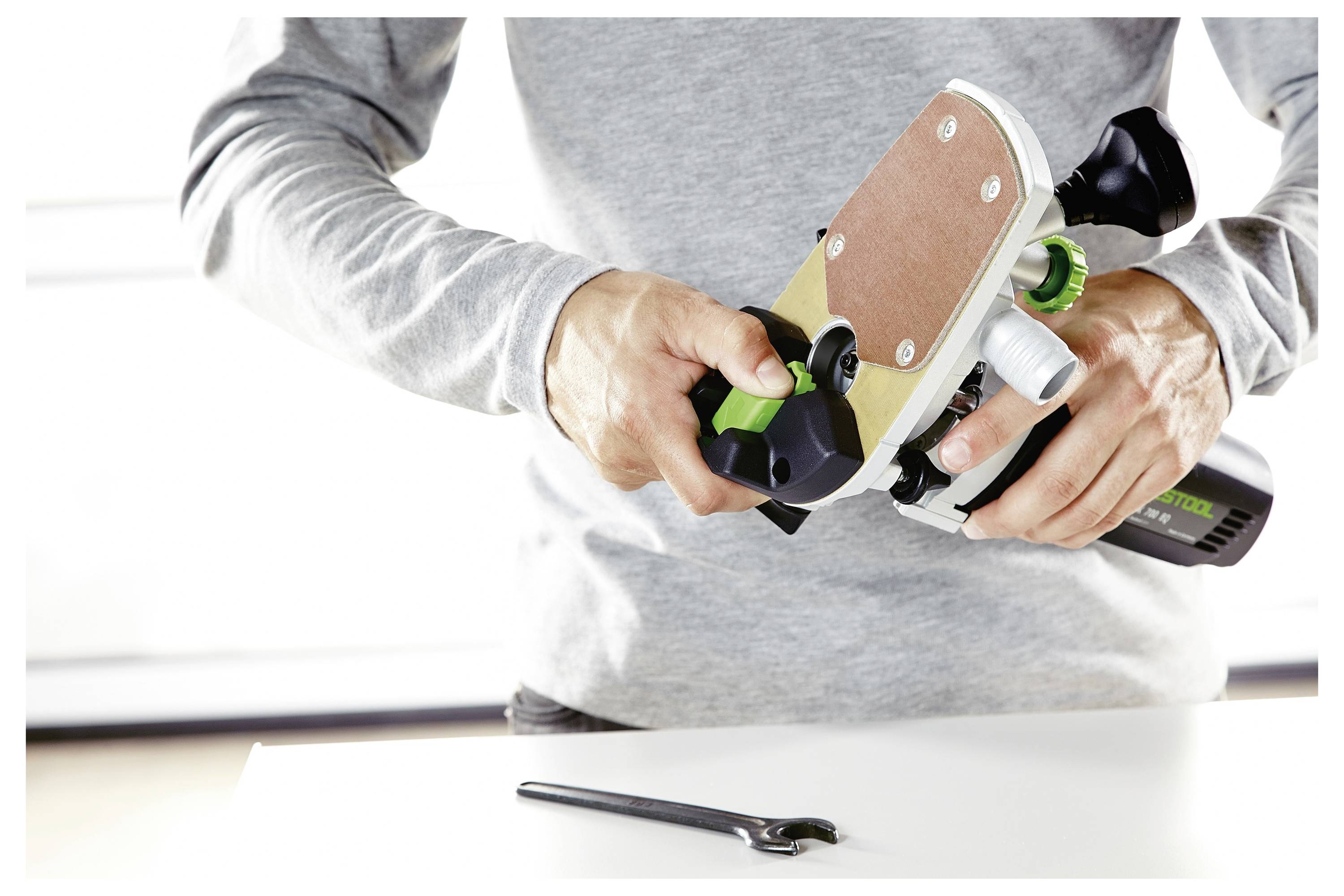 Eine Person stellt ein Holzbearbeitungswerkzeug auf einem Tisch ein, mit einem Schraubenschlüssel in der Nähe, was auf Werkzeugwartung oder -einstellung hindeutet.