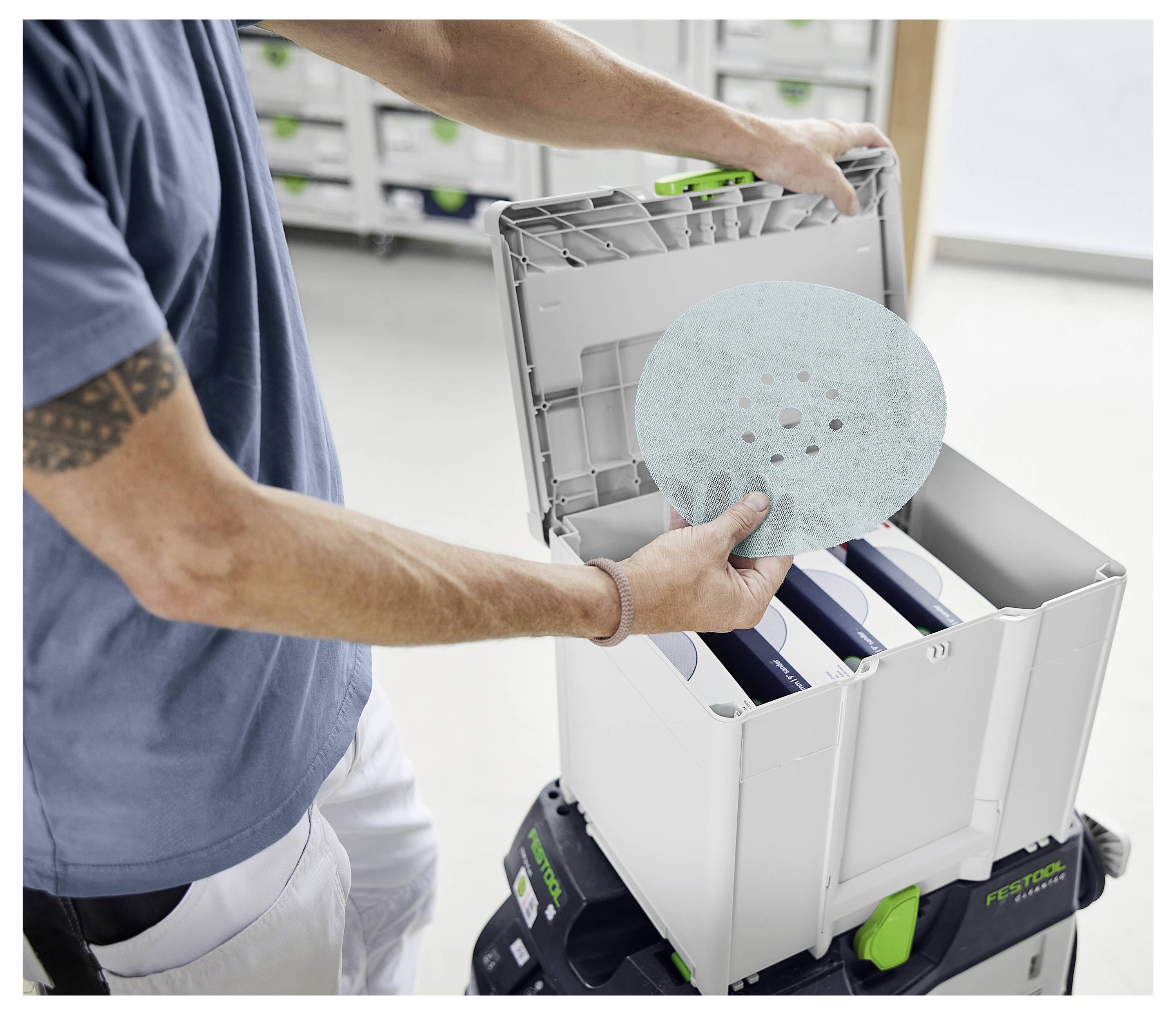 Verschiedene Stapel von runden und dreieckigen Schleifpapierscheiben in Hellblau mit Löchern sind auf weißem Hintergrund angeordnet.