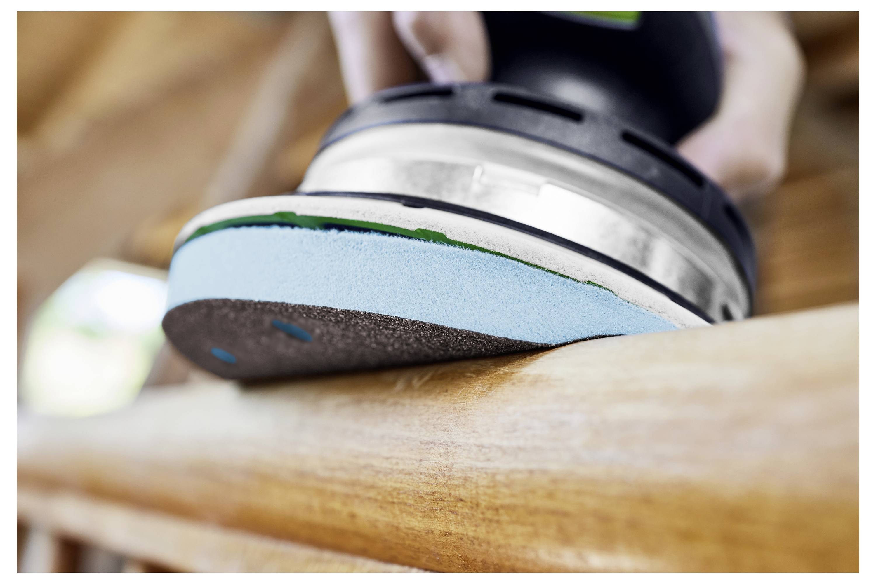 Eine Person stellt ein tragbares Elektrowerkzeug mit angebrachtem Staubsack ein und bereitet sich wahrscheinlich auf eine Holzbearbeitungsaufgabe vor. Der Hintergrund zeigt eine Werkstattumgebung.