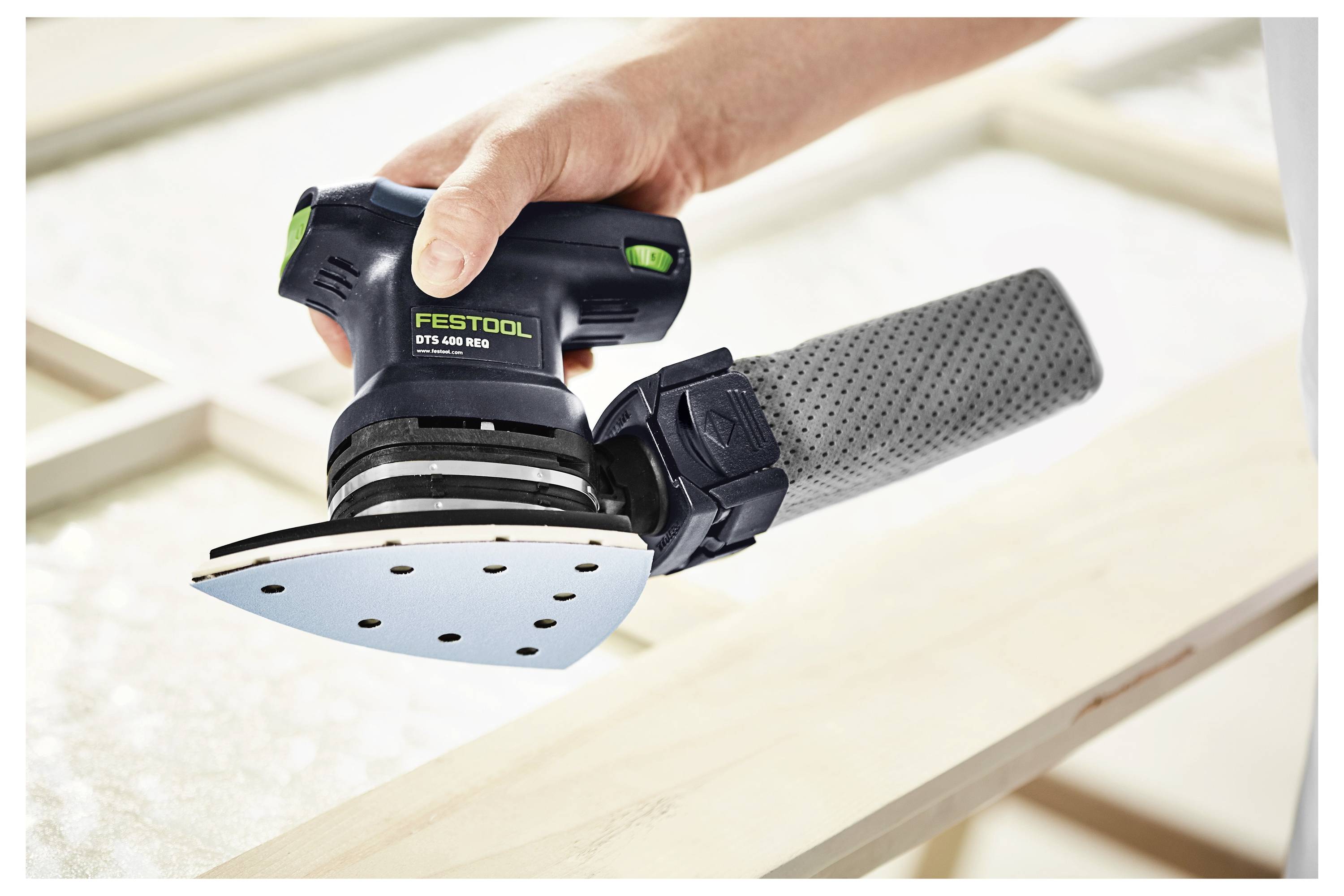 Eine Person hält einen tragbaren Elektroschleiffer und glättet eine Holzoberfläche, wobei das ergonomische Design des Werkzeugs und der Benutzergriff hervorgehoben werden.