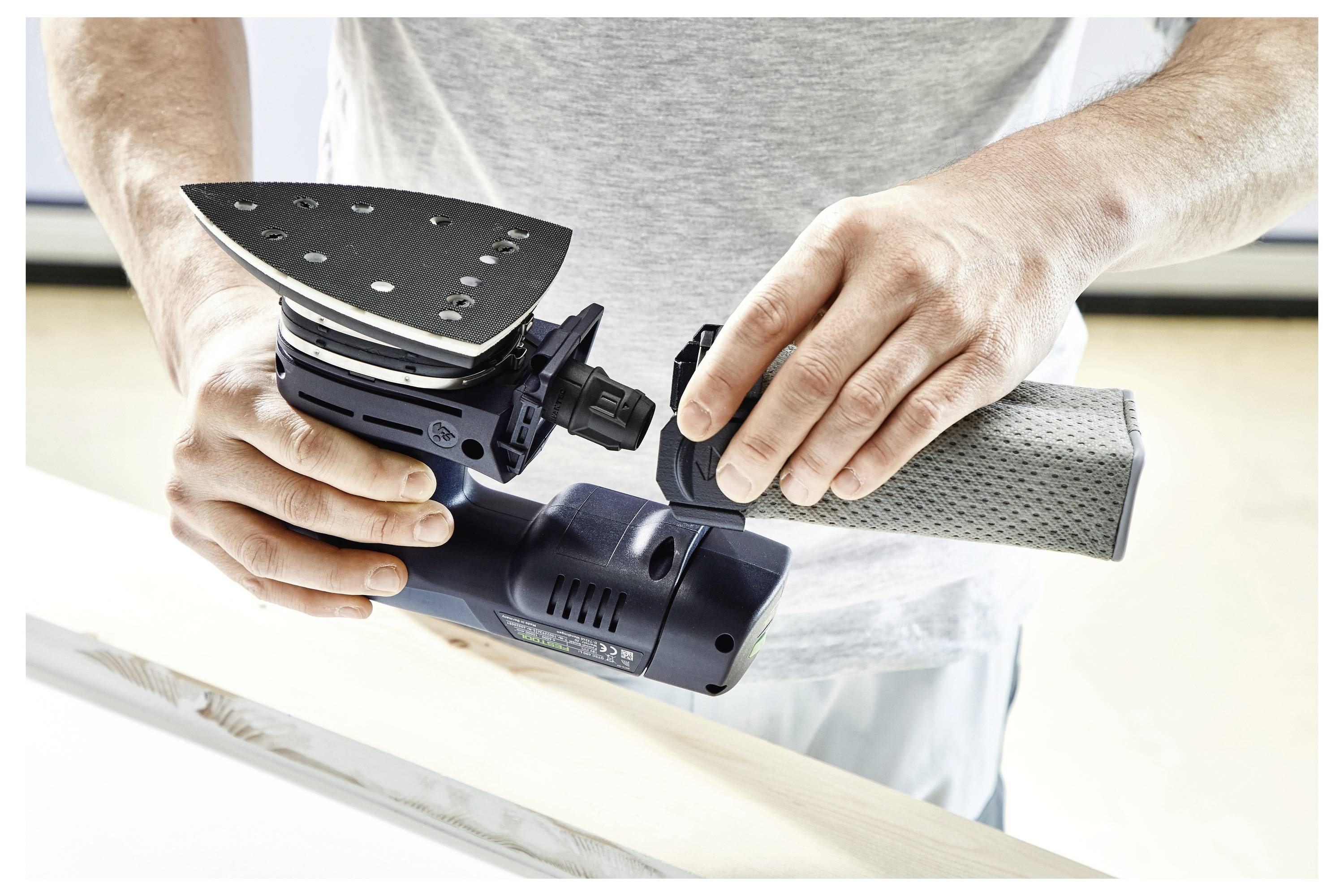 Eine Person hält ein Elektrowerkzeug mit einem angebrachten Schleifteller und demonstriert dessen Verwendung auf einer Holzoberfläche in Innenräumen.