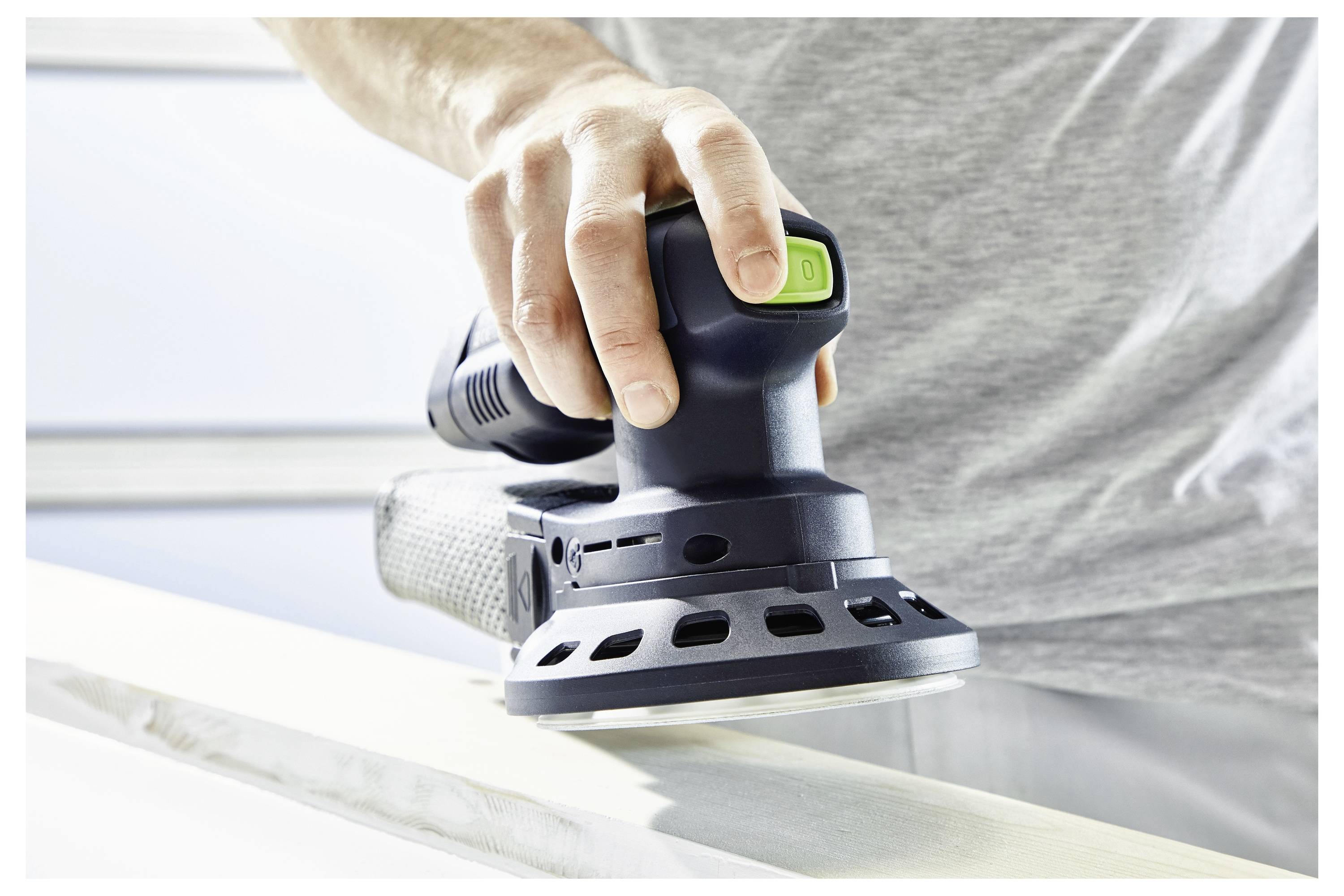 Ein Festool-Akkupack mit einem Ladekabel auf einer hell gefärbten Oberfläche, unscharfer Hintergrund mit Werkstattwerkzeugen.