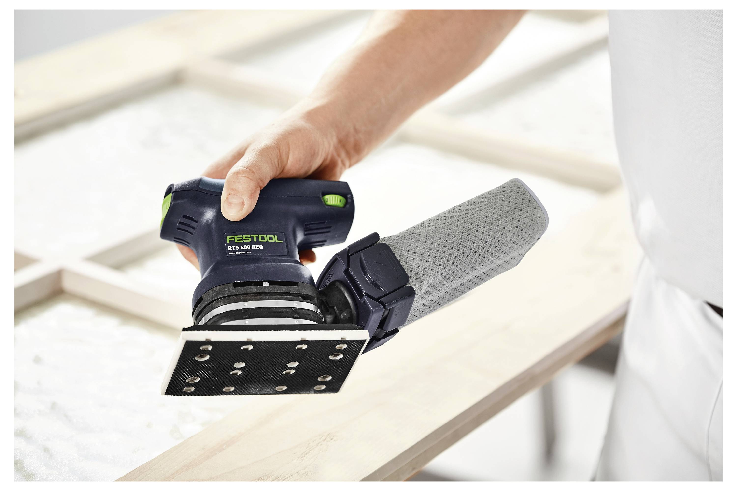 Person, die einen Festool RTS 400 REQ Schleifer auf einer Holzoberfläche verwendet, wobei der Fokus auf sanftes Schleifen und präzise Kontrolle liegt.