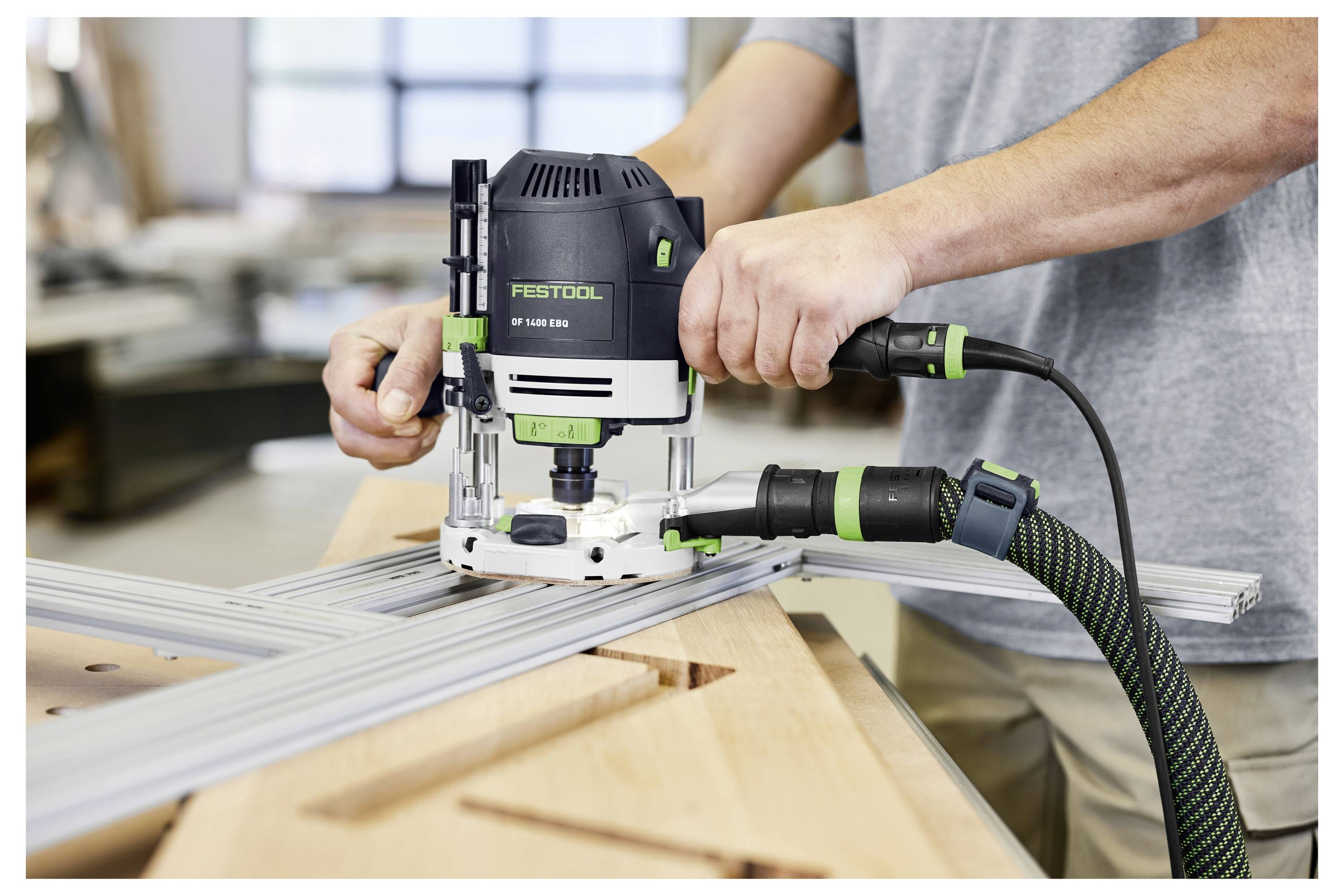 Eine Hand hält einen Festool-Elektroschleiffer und glättet eine Holzoberfläche. Das Werkzeug verfügt über einen grünen Knopf und einen strukturierten Griff.