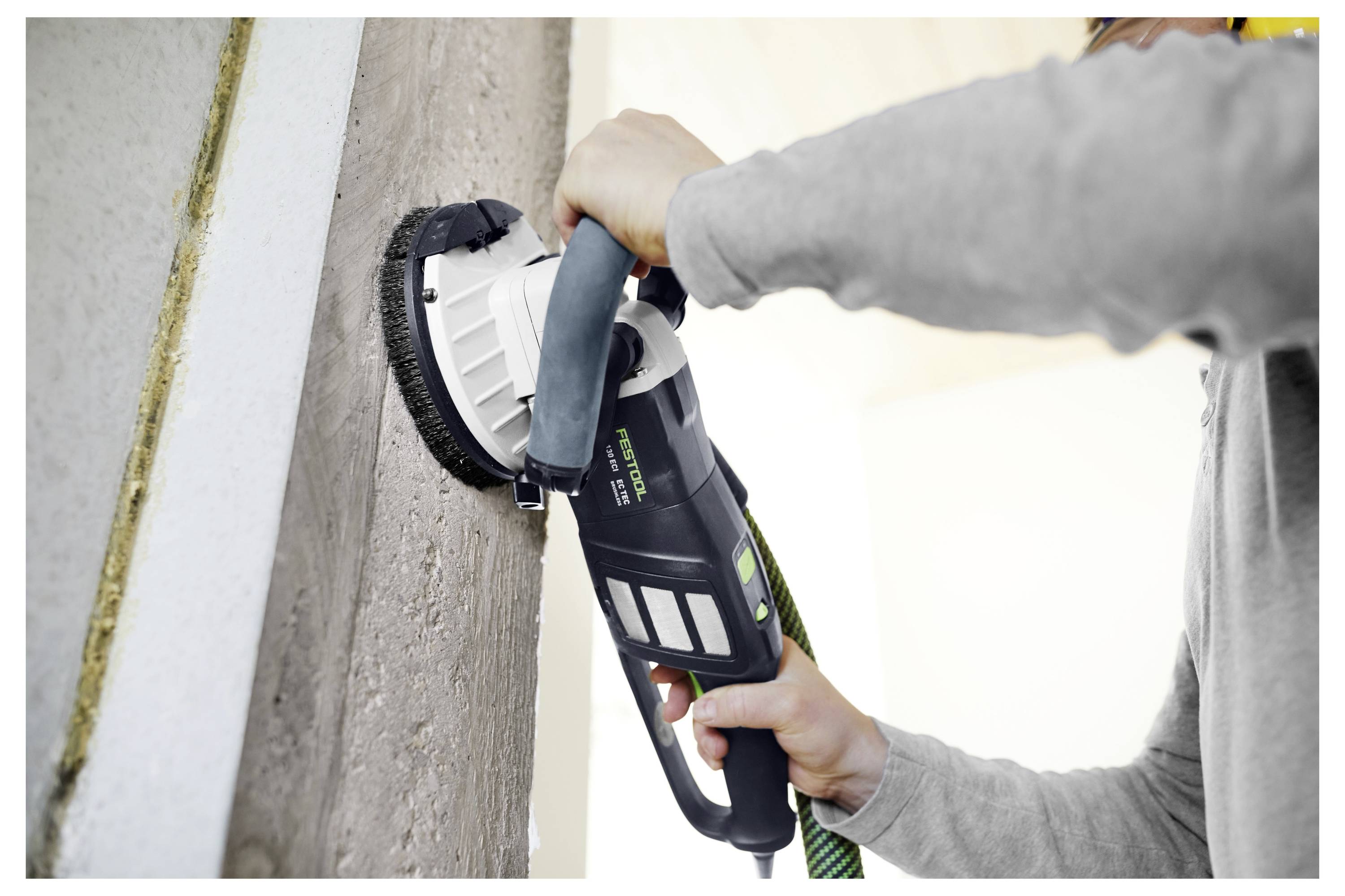 Eine Person verwendet einen elektrischen Wandschlifer auf einer Betonwand und glättet die Oberfläche.