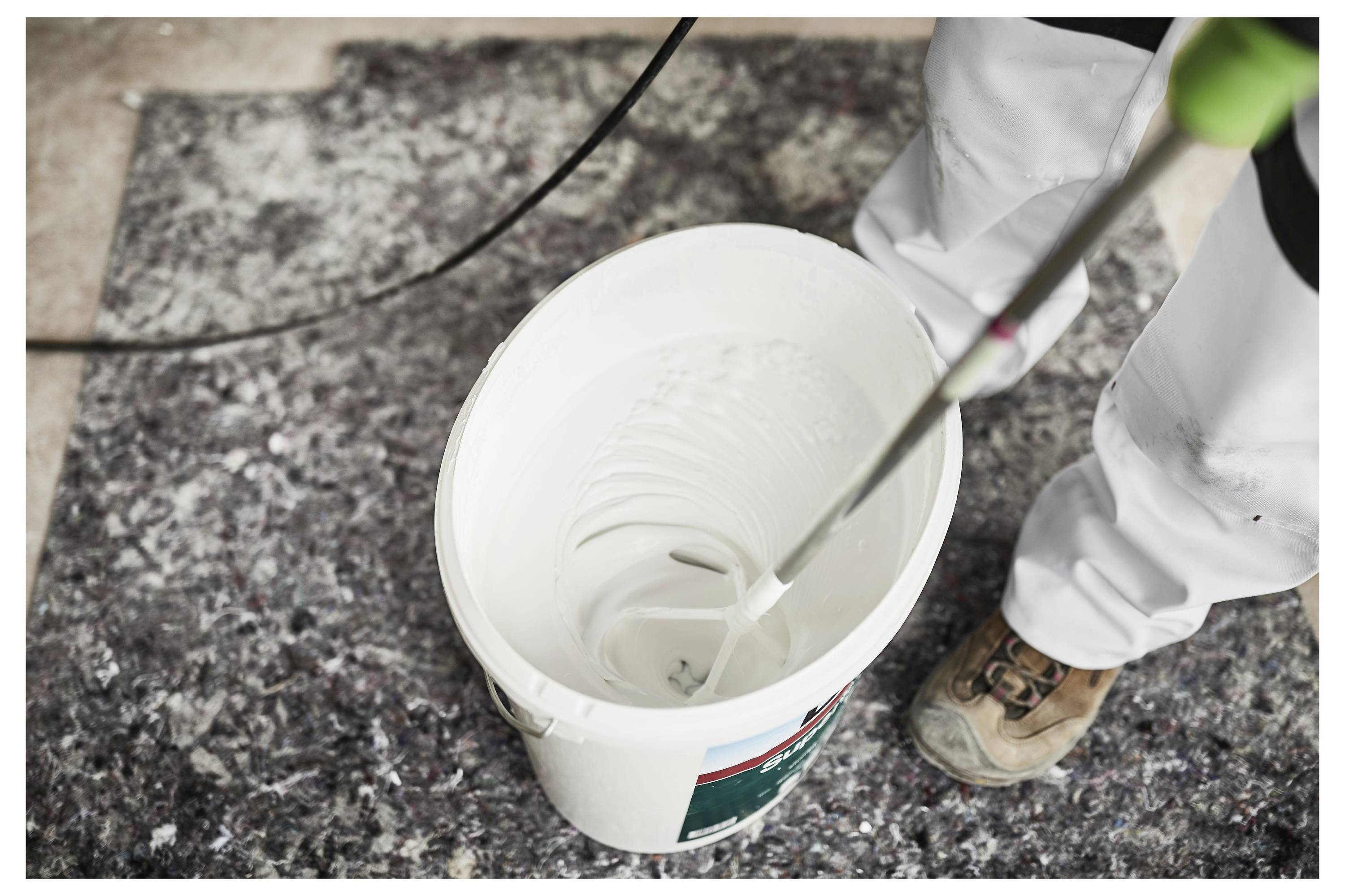 Eine Person verwendet einen Akkubohrer, um eine Schraube in ein Holzbrett einzudrehen, mit mehreren Schrauben und einem fertigen Holzrahmen im Hintergrund.