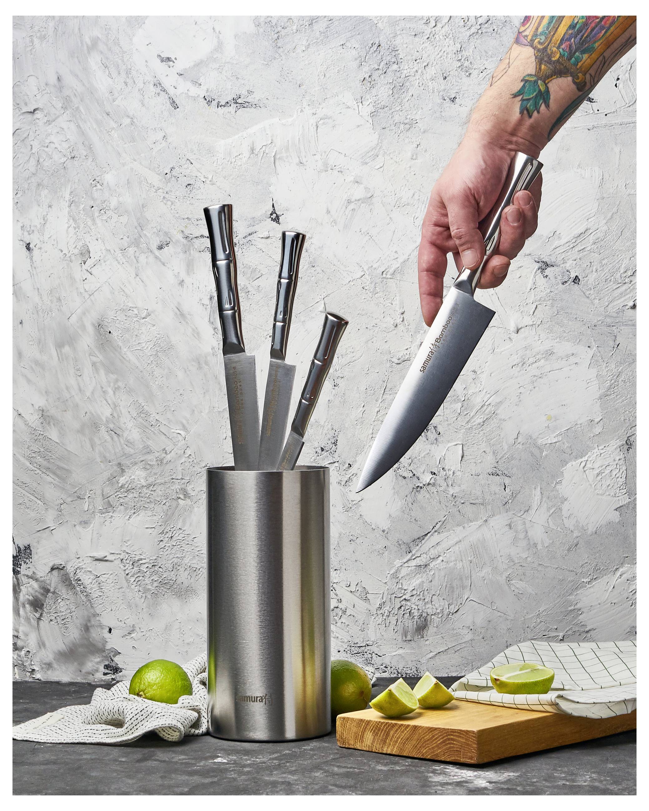 'A hand holding a chef's knife is removing it from a knife block containing four other knives. Lemons and a checkered cloth are nearby.'