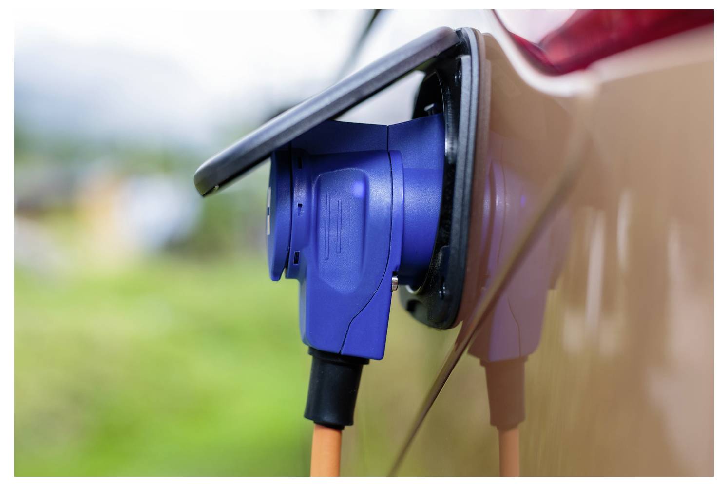 Blauer Elektrofahrzeug-Ladestecker, der mit dem Ladeanschluss eines Autos im Freien verbunden ist.