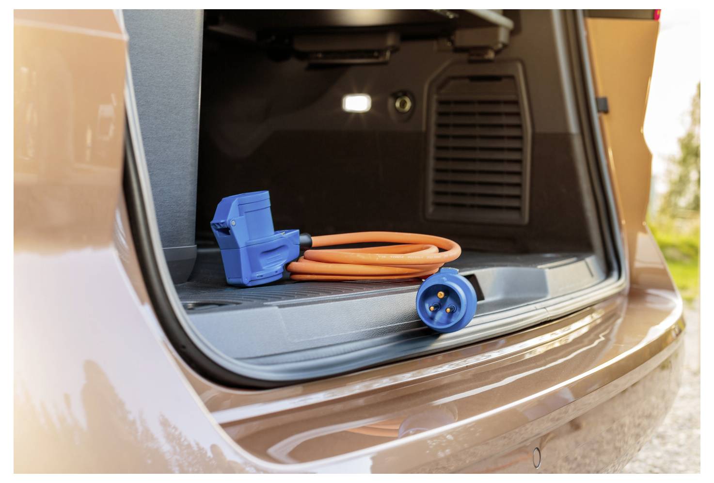 Ein Elektroautoladeabel mit einem blauen Stecker befindet sich im offenen Kofferraum eines Fahrzeugs und deutet auf Einsatzbereitschaft oder Lagerung hin.
