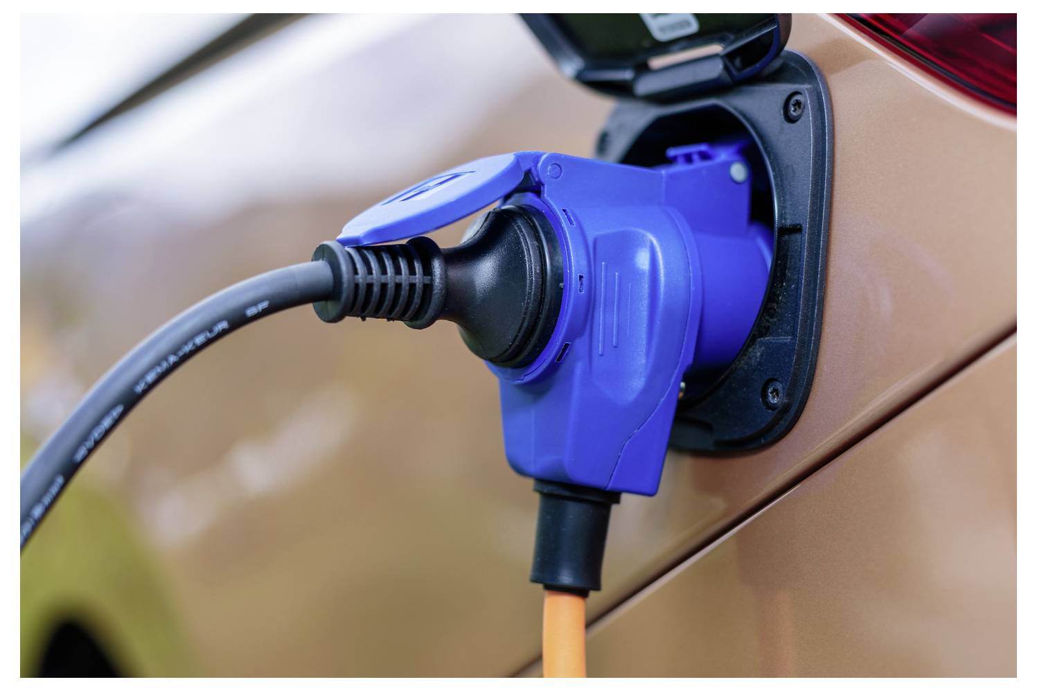 Nahaufnahme eines blauen Ladesteckers für Elektrofahrzeuge, der mit dem Ladeanschluss des Autos verbunden ist.