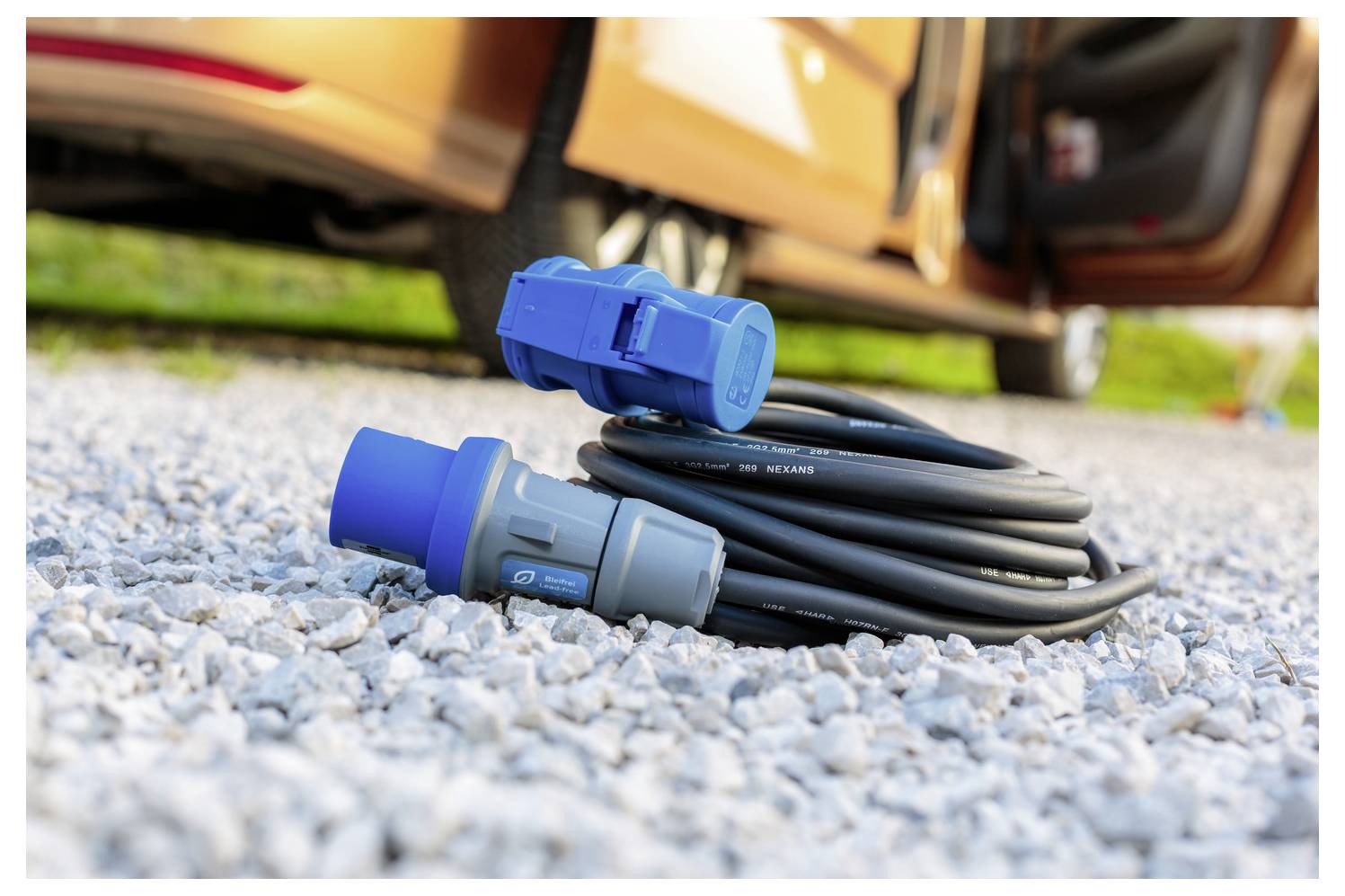 Elektrofahrzeug-Ladekabel aufgerollt auf Kiesgrund, mit offener Autotür im Hintergrund.