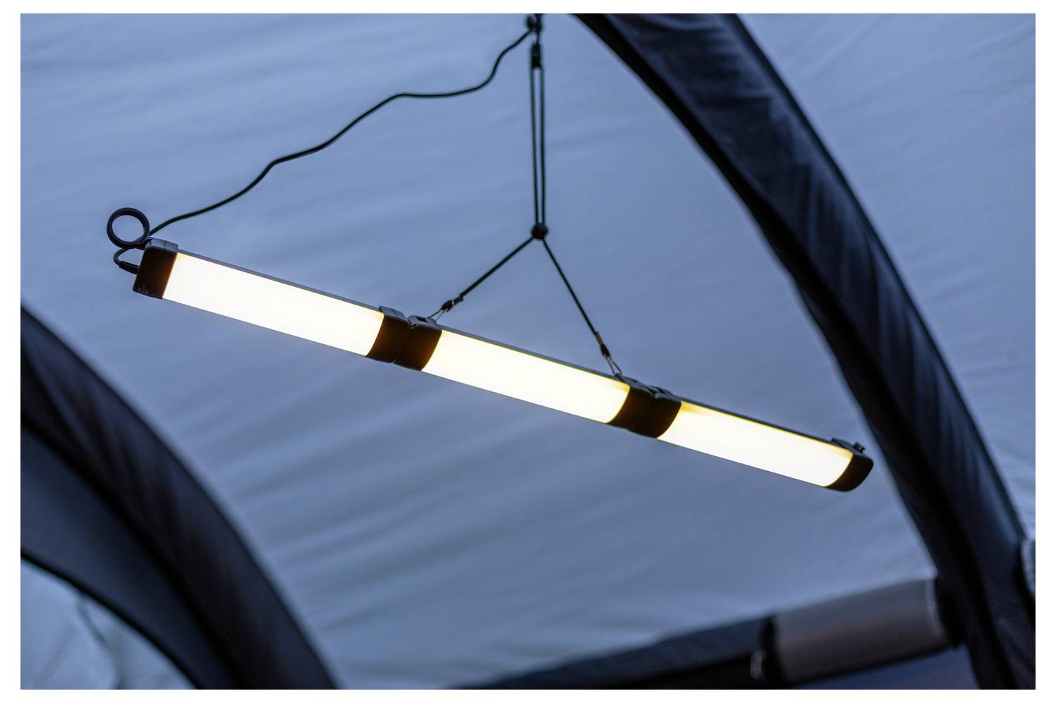 Eine Reihe von drei leuchtenden Leuchtstoffröhren, die von einer Decke hängen und industrielle Beleuchtung in einer Innenraumeinstellung zeigen.