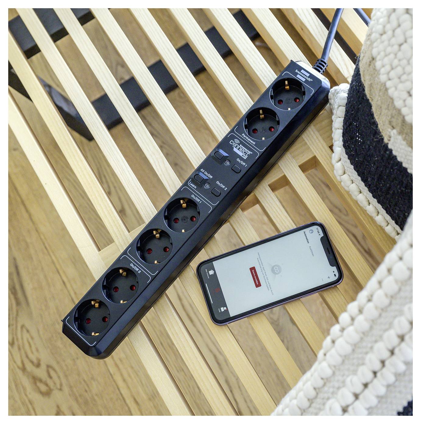 Eine intelligente Steckdosenleiste mit vier Steckdosen ist auf einer Holzlattenfläche neben einem Smartphone platziert, das die App „Smart Life