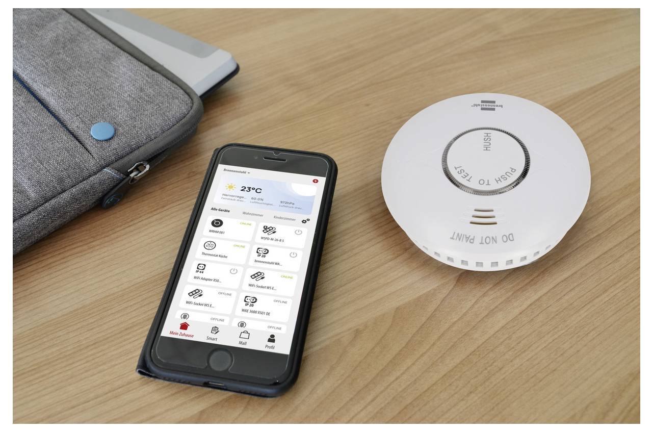 Ein Smartphone, das eine Wetter-App anzeigt, neben einem Rauchmelder auf einem Holztisch, was auf Smart-Home-Verwaltung hindeutet.