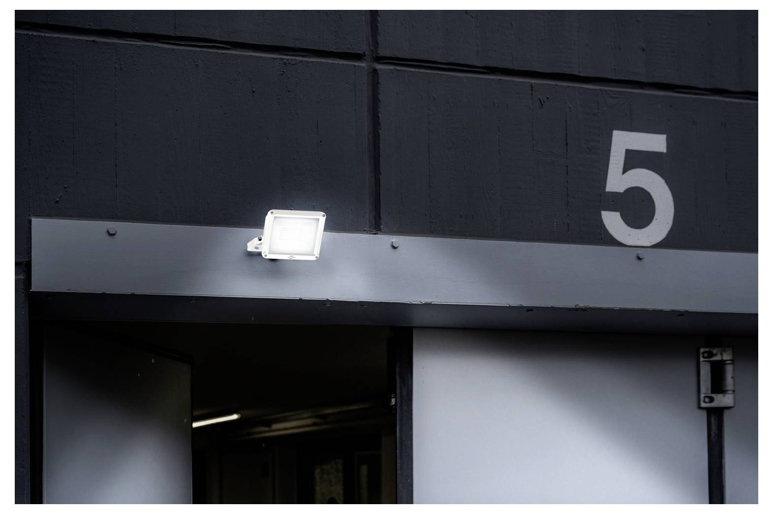 Gebäudeeingang mit der Nummer 5 über der Türöffnung markiert, mit einem kleinen Außenlicht an der Fassade angebracht.