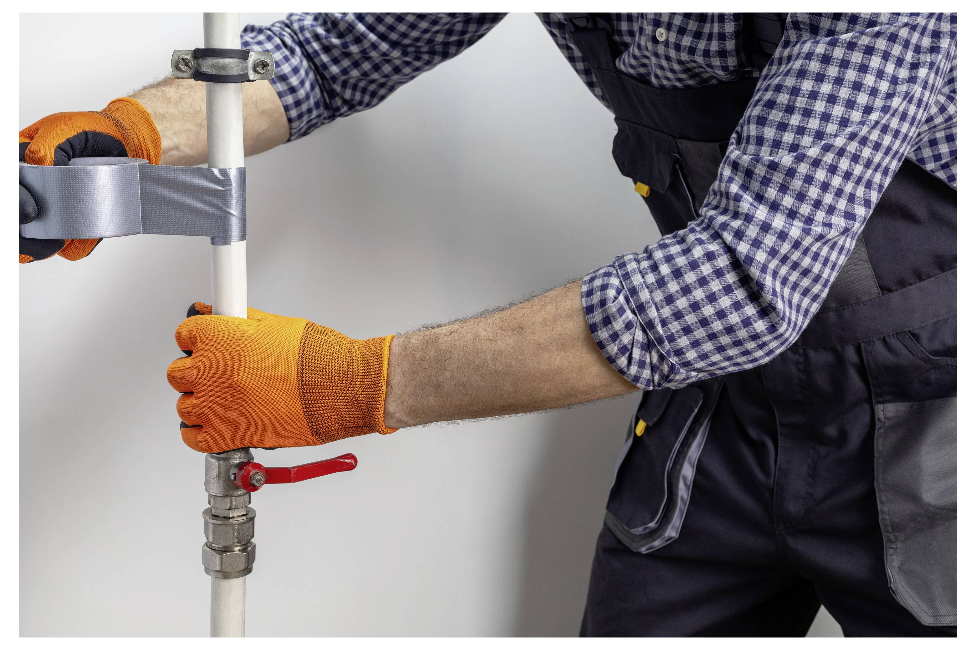Arbeiter mit Handschuhen, der eine Metallrohrschelle an einem vertikalen weißen Rohr mit einem Schraubenschlüssel anzieht, was auf eine Installation oder Reparatur von Rohrleitungen hindeutet.