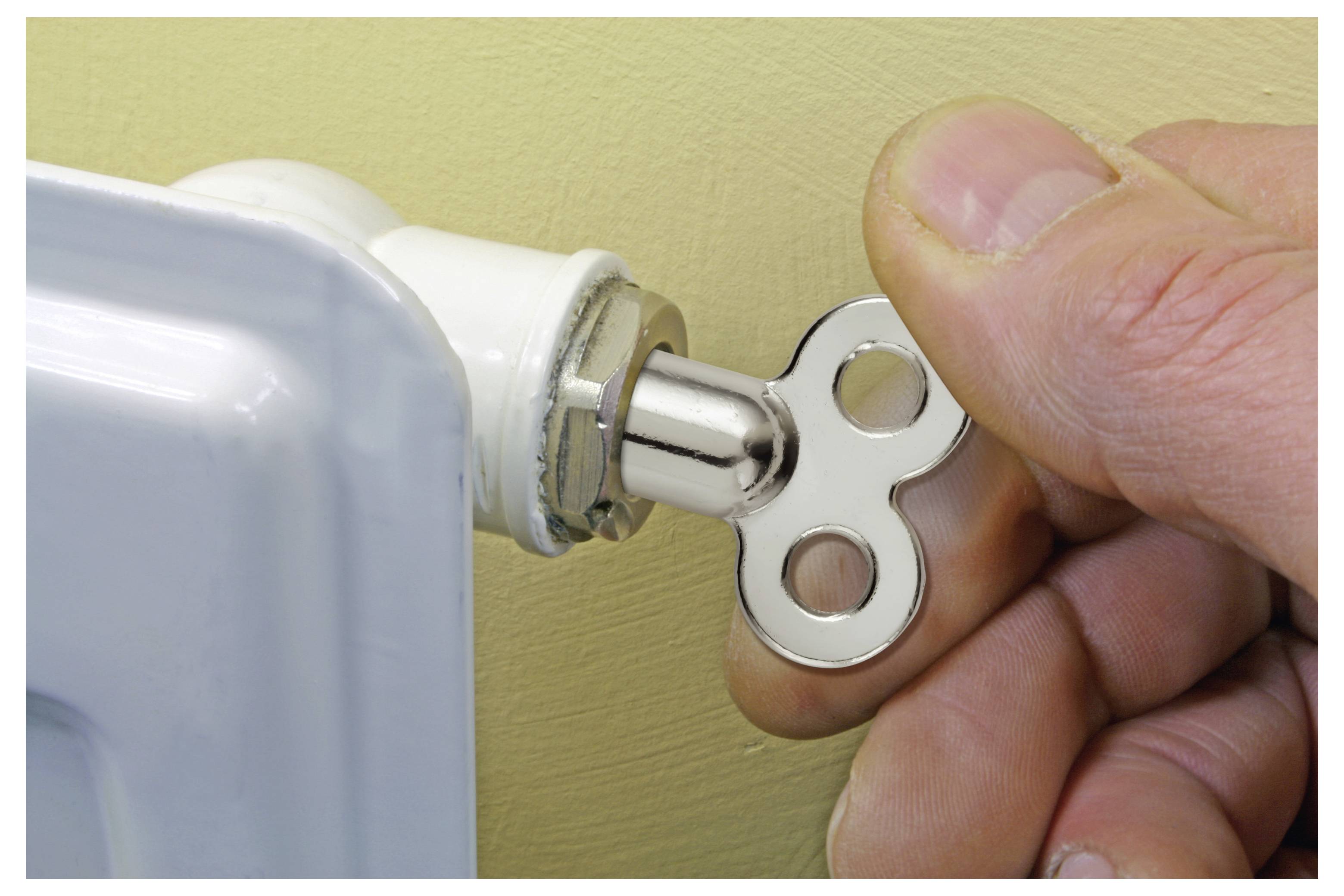 Hand, die einen Schlüssel verwendet, um ein Heizkörperventil an einem Metalltafelheizer zu öffnen oder festzuziehen.