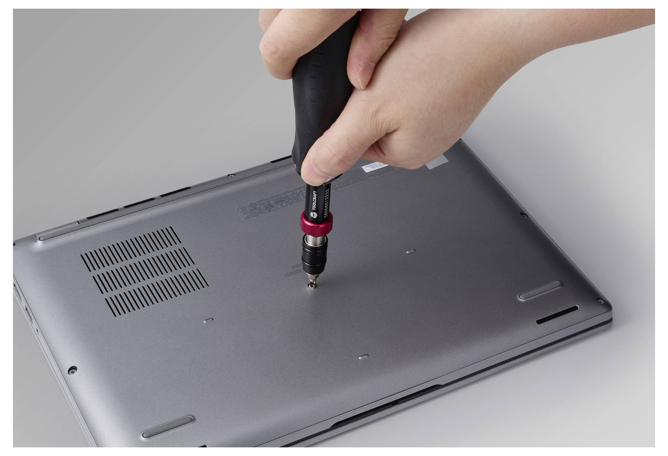 Hände schrauben mit einem Schraubendreher das untere Panel eines Laptops ab.