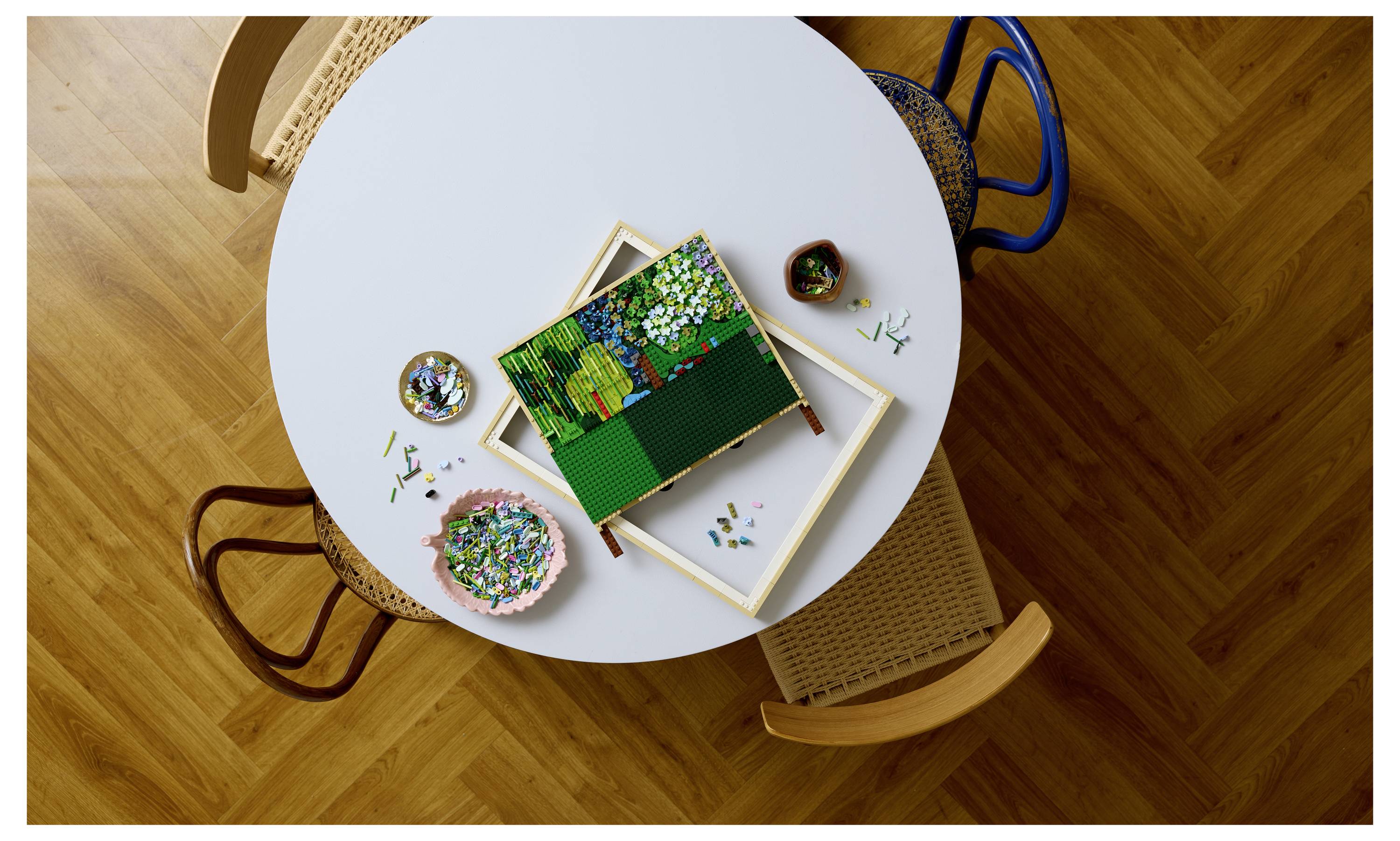 Drei Stühle um einen runden Tisch, auf dem ein teilweise gelöstes Puzzle liegt, Teile sind um den Tisch verstreut und Behälter enthalten zusätzliche Teile.