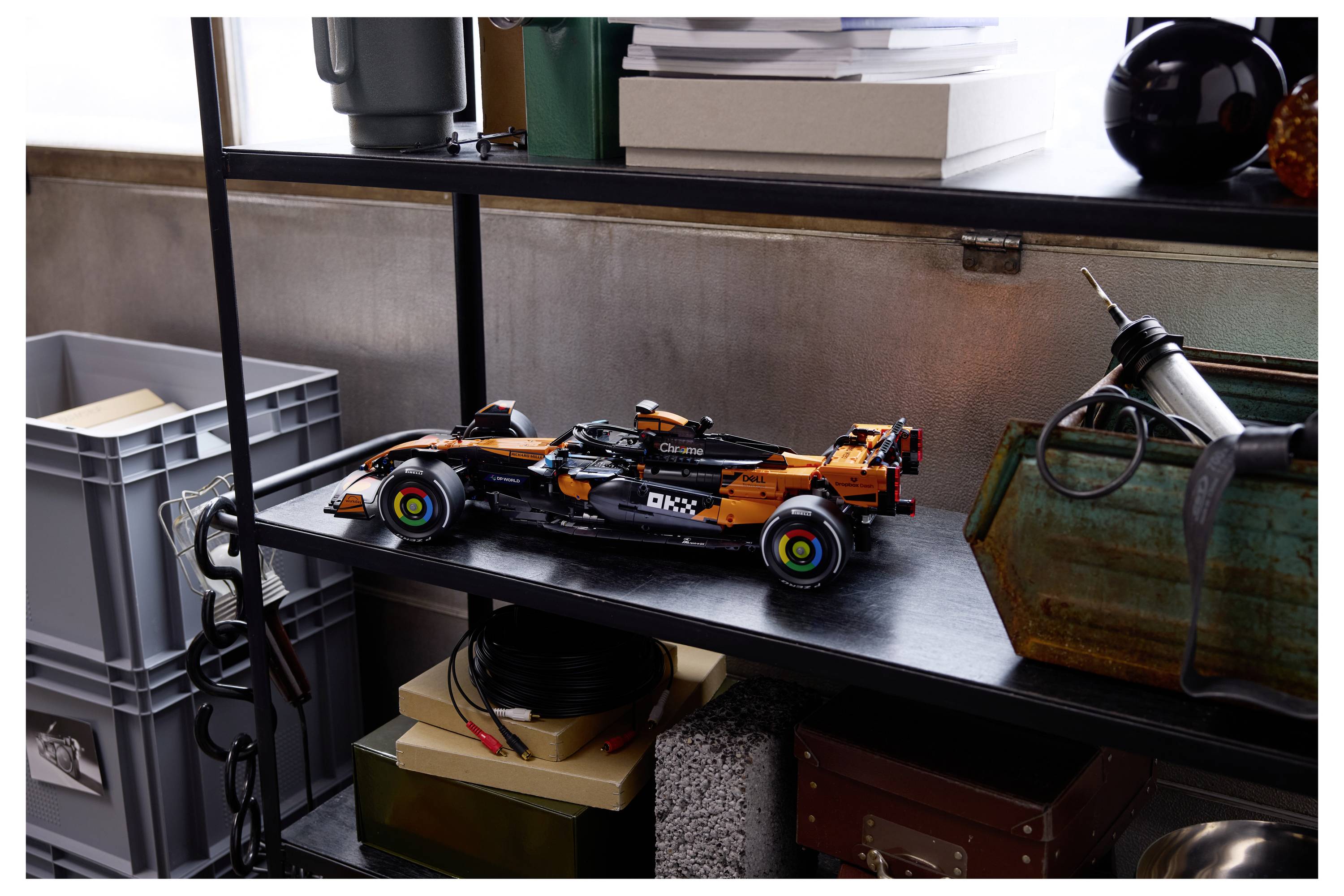Model Formel-1-Rennwagen auf einem Regal ausgestellt, umgeben von Lagerkisten, Büchern und Werkzeugen, was eine werkstattähnliche Umgebung schafft.