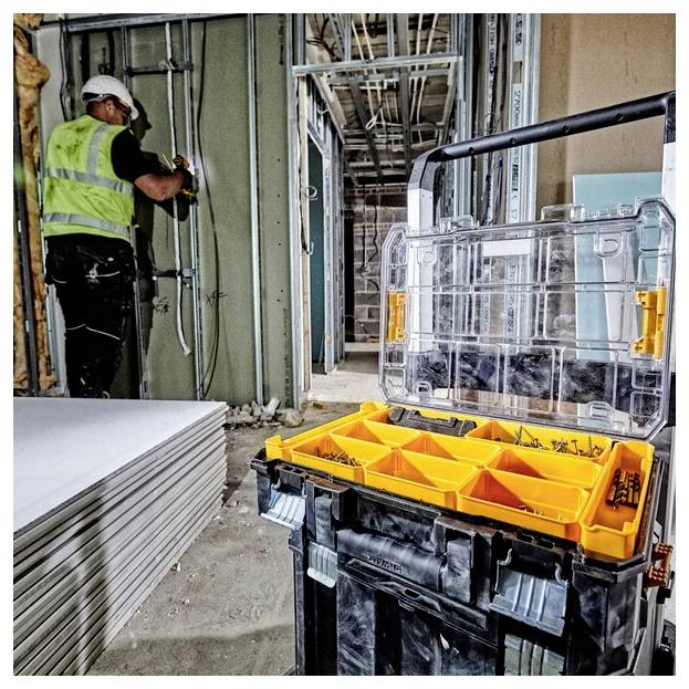 Ein Bauarbeiter in einer Sicherheitsweste installiert Leitungen in einer Wandkonstruktion in einem im Bau befindlichen Gebäude, mit einer Werkzeugkiste in der Nähe.