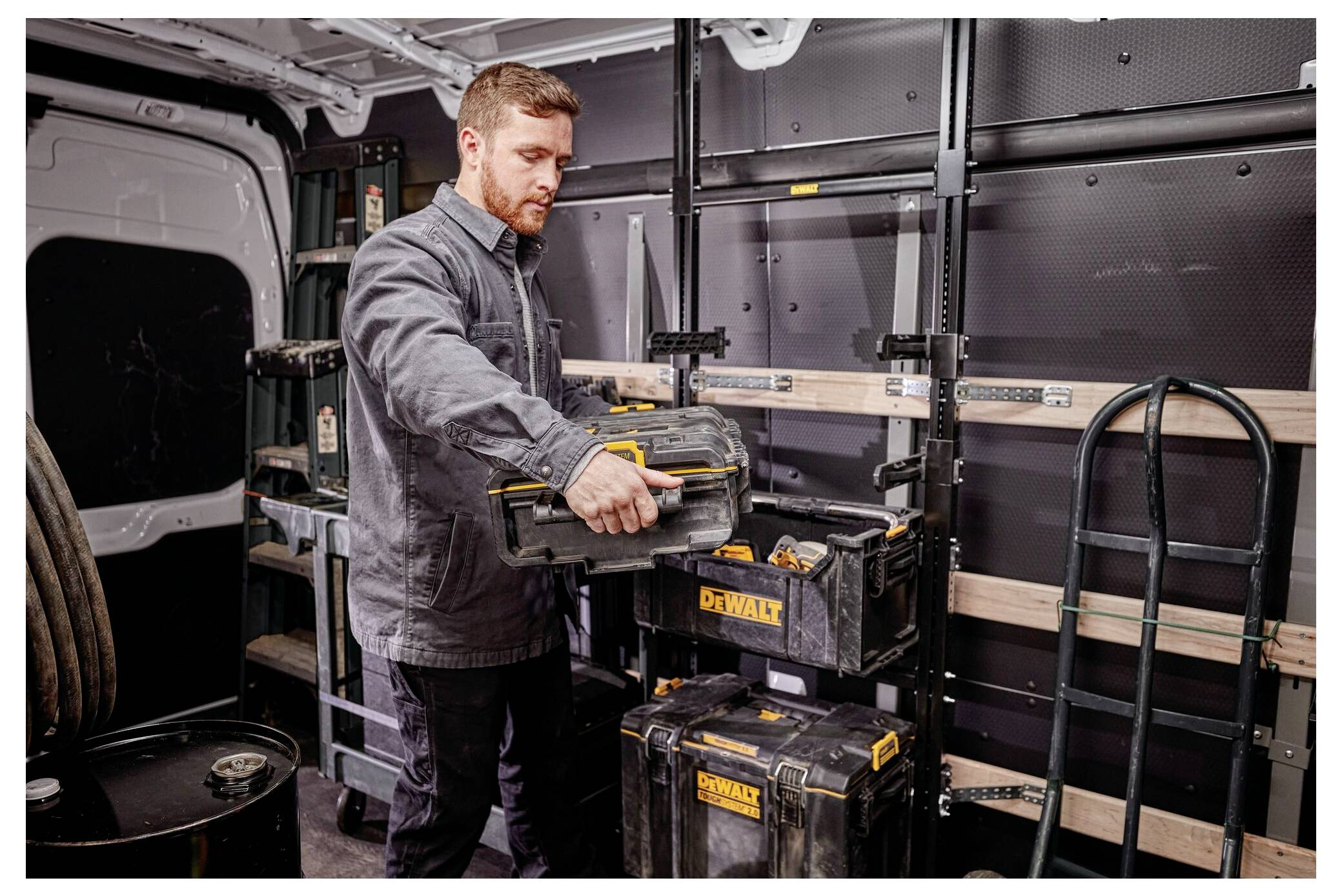 Eine Person organisiert Werkzeuge in einem Lieferwagen und platziert einen schwarz-gelben Werkzeugkoffer auf einem Regal. Das Innere zeigt organisierte Lagerlösungen.