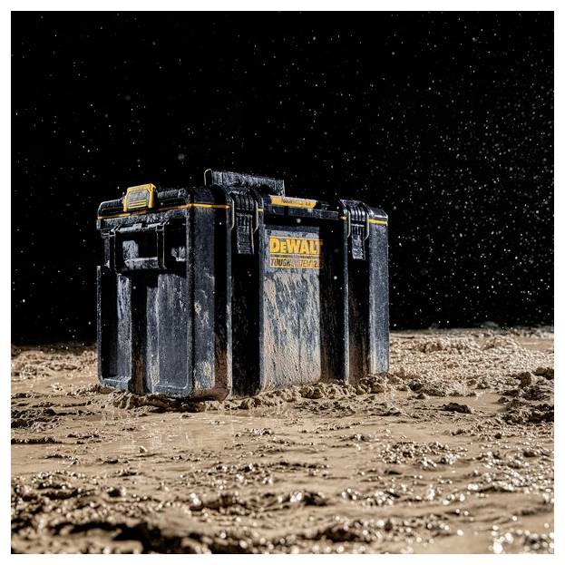 Ein mit Schlamm bedeckter schwarz-gelber Werkzeugkasten sitzt auf nassem, schlammigem Boden mit Wasser, das herum spritzt, und zeigt sein robustes, wasserdichtes Design.