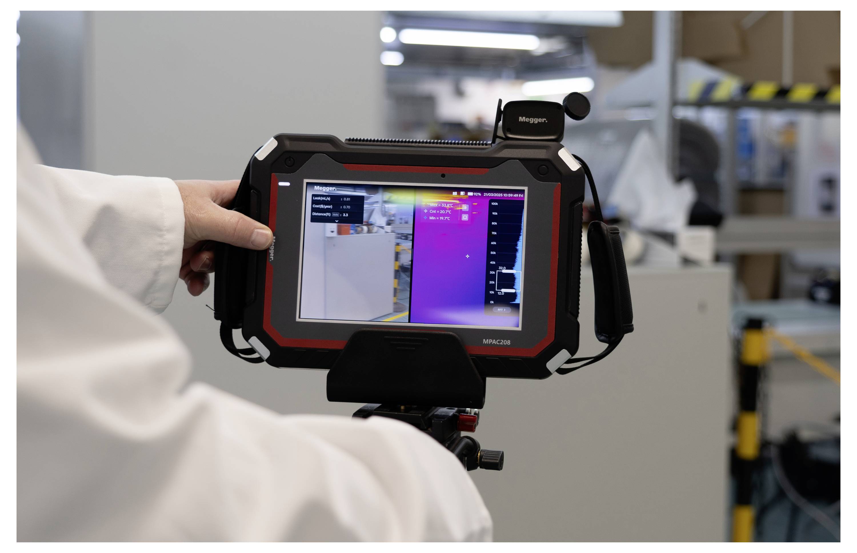 Eine Person in einem Laborkittel hält ein Wärmebildgerät, das eine farbcodierte Wärmekarte auf dem Bildschirm anzeigt, das zur Überwachung der Ausrüstungstemperatur verwendet wird.