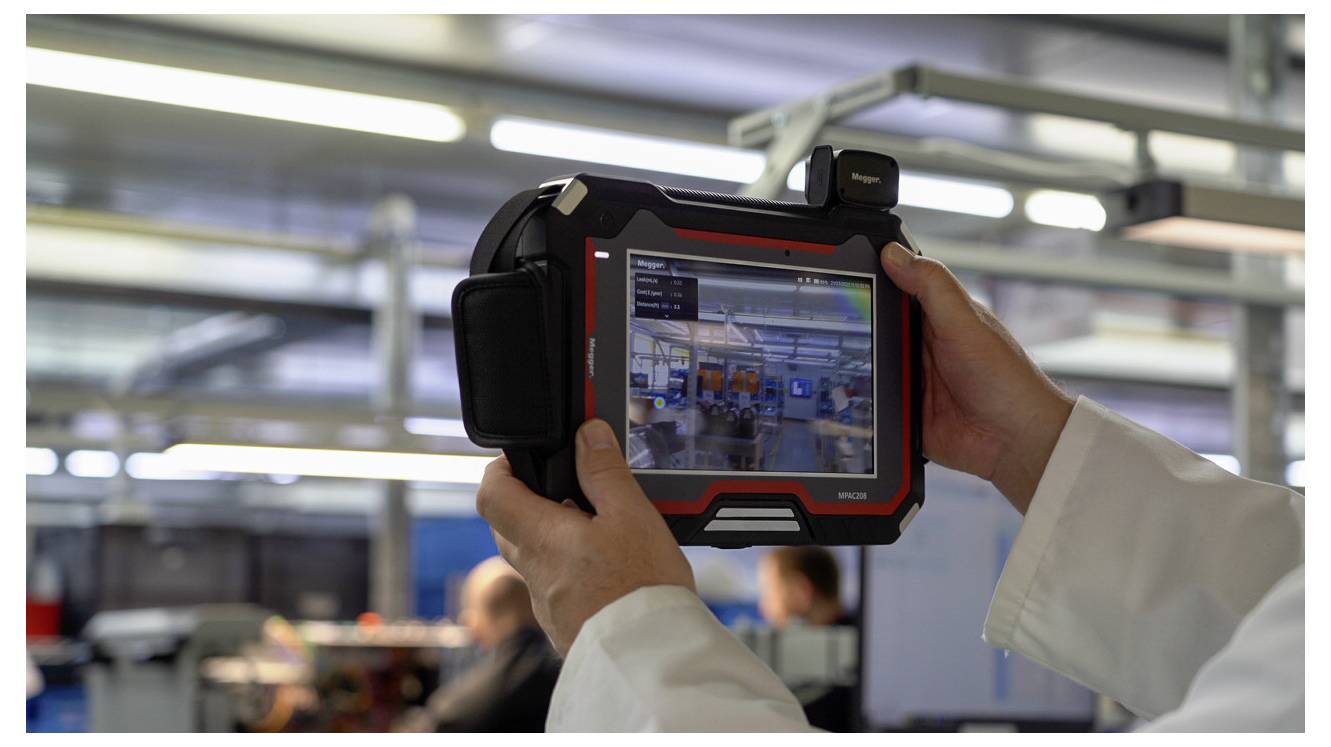 Person im Laborkittel hält ein Tablet-Gerät, das eine digitale Benutzeroberfläche anzeigt und ein Live-Bild des Inneren einer Produktionsanlage erfasst.