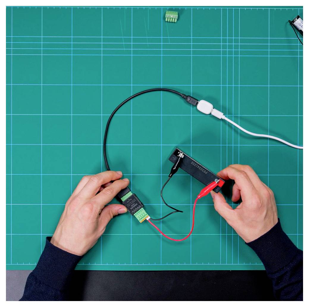 Hände verbinden Drähte mit elektronischen Komponenten auf einer blauen Matte mit Rastermuster, was einen elektronischen Schaltungsaufbau demonstriert.