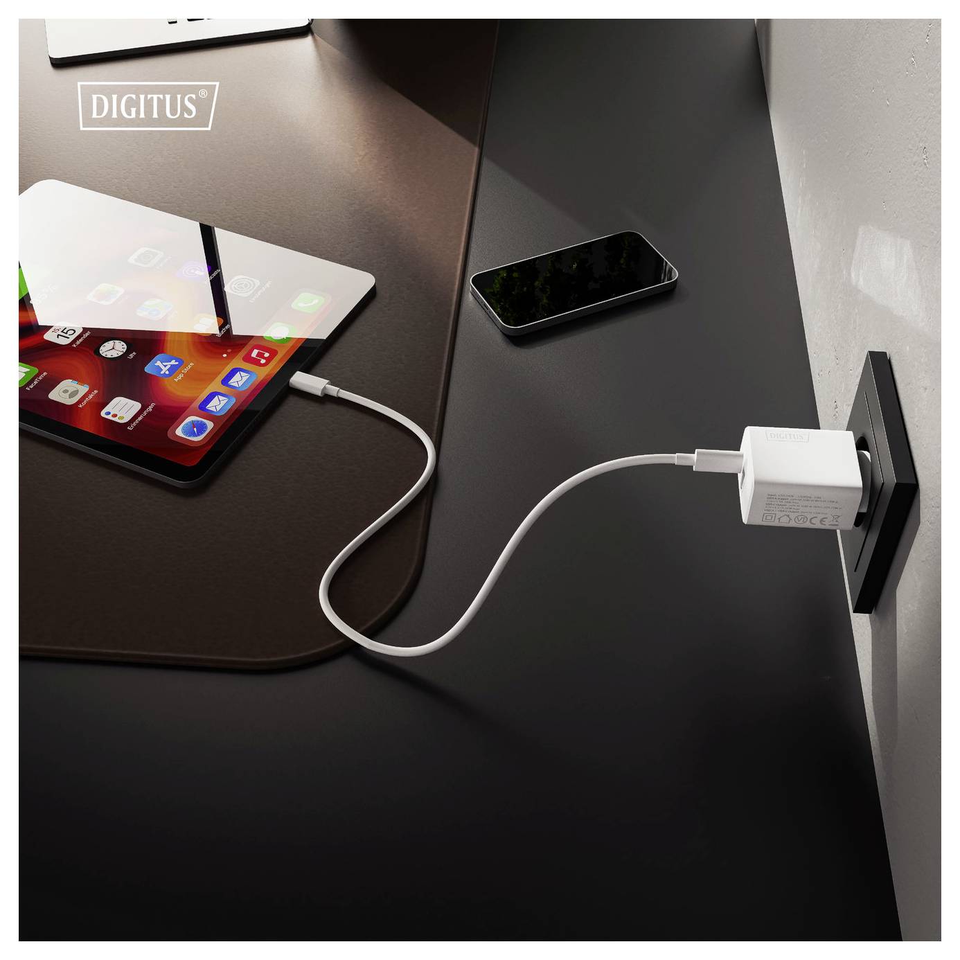 Ein Tablet und ein Smartphone auf einem Schreibtisch, wobei das Tablet über ein USB-Kabel mit einem Wandladegerät verbunden ist.