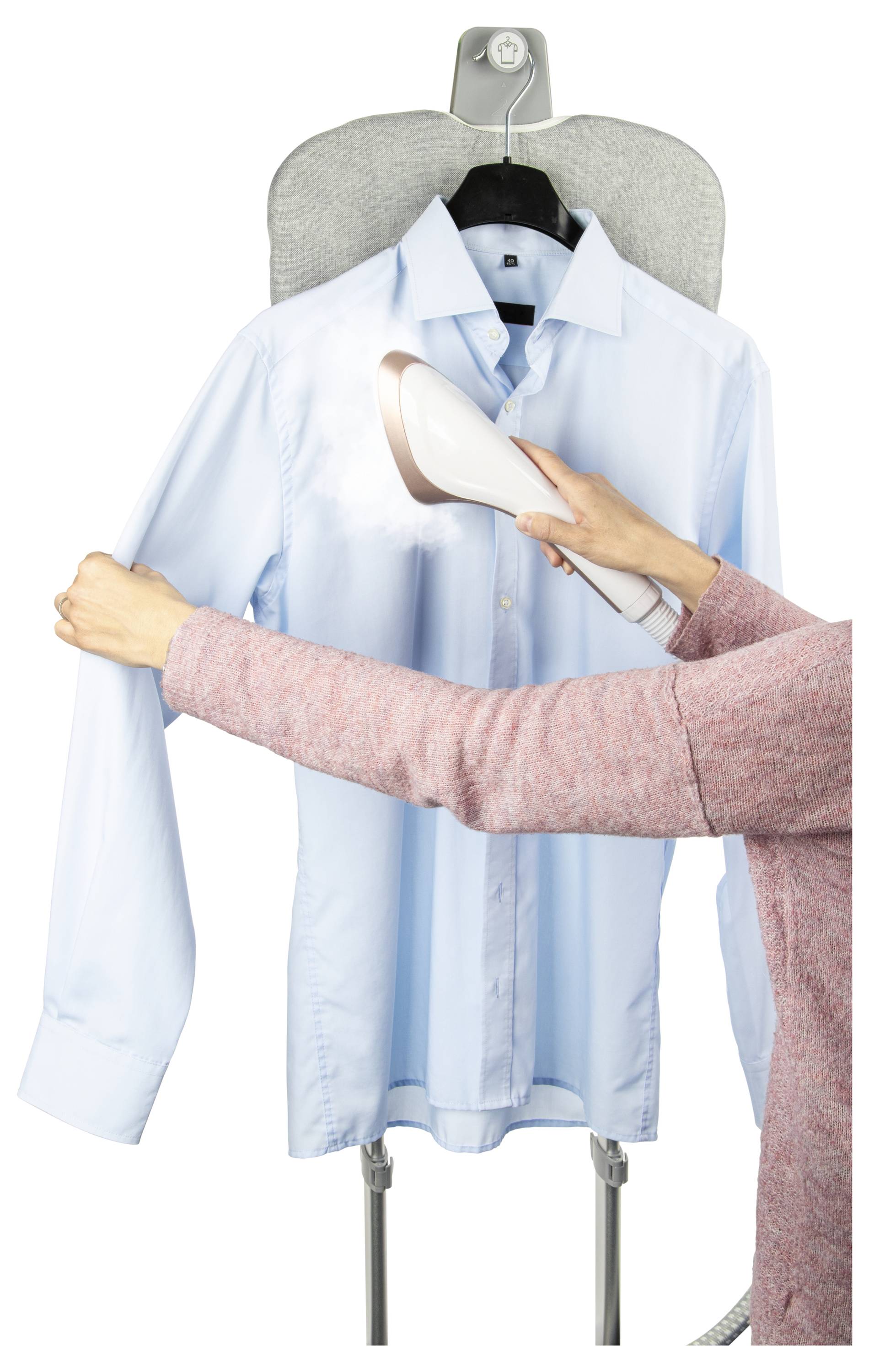 Eine Person verwendet einen tragbaren Dampfreiniger auf einem blauen Hemd, das auf einem Bügelbrett hängt, und gibt Dampf ab, um Falten zu entfernen.