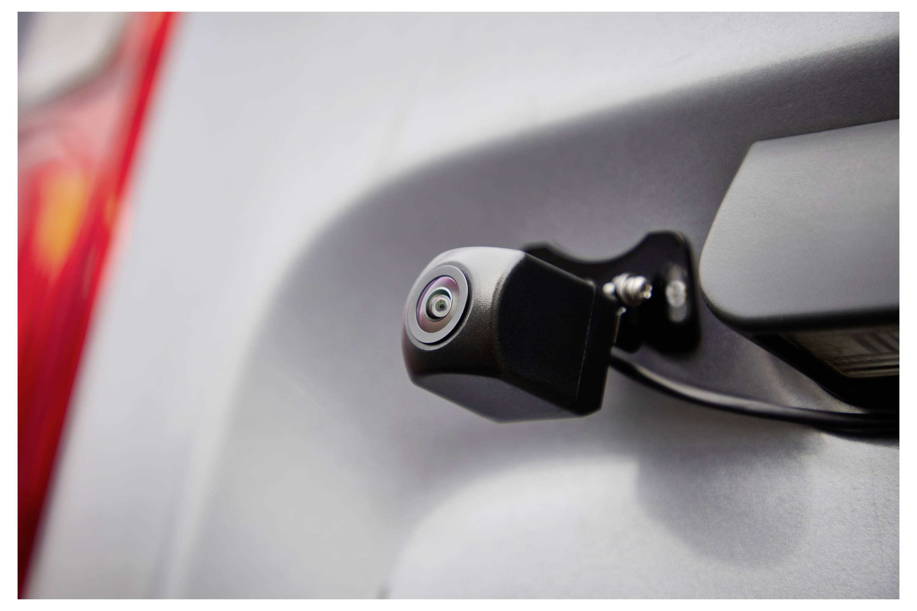 Eine Nahaufnahme einer Rückfahrkamera eines Fahrzeugs, die in der Nähe des hinteren Griffs angebracht ist und ihre Rolle bei der Unterstützung von Rückwärtsbewegungen hervorhebt.