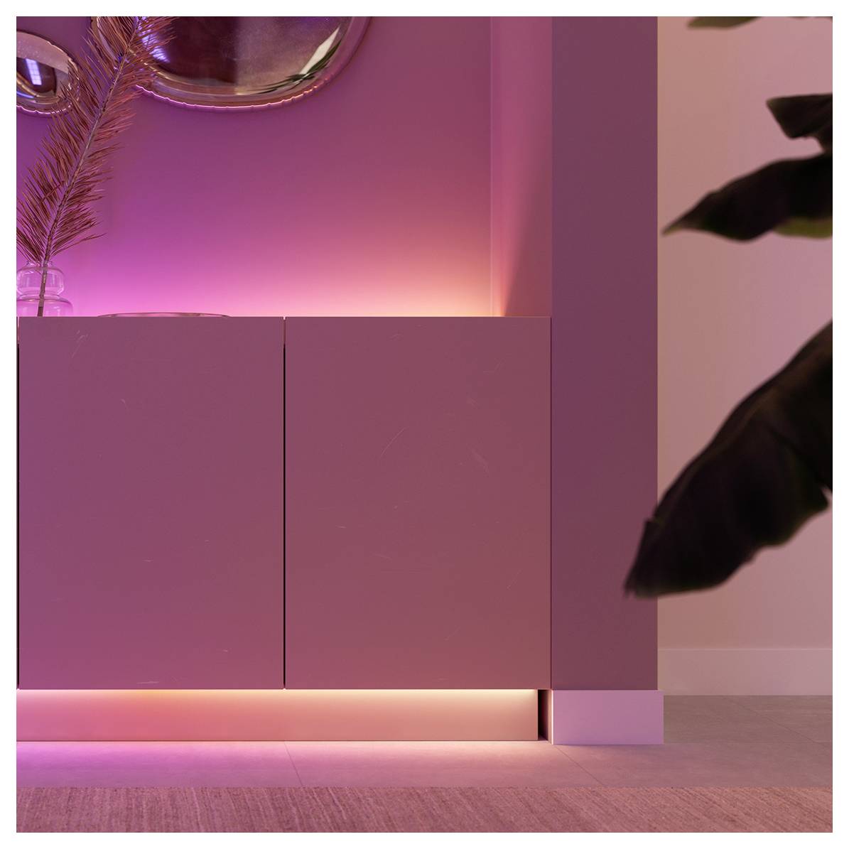 Ein modernes, minimalistisches Sideboard mit rosafarbener Akzentbeleuchtung darunter, an einer sanften rosafarbenen Wand platziert. Blätter einer Pflanze teilweise sichtbar.
