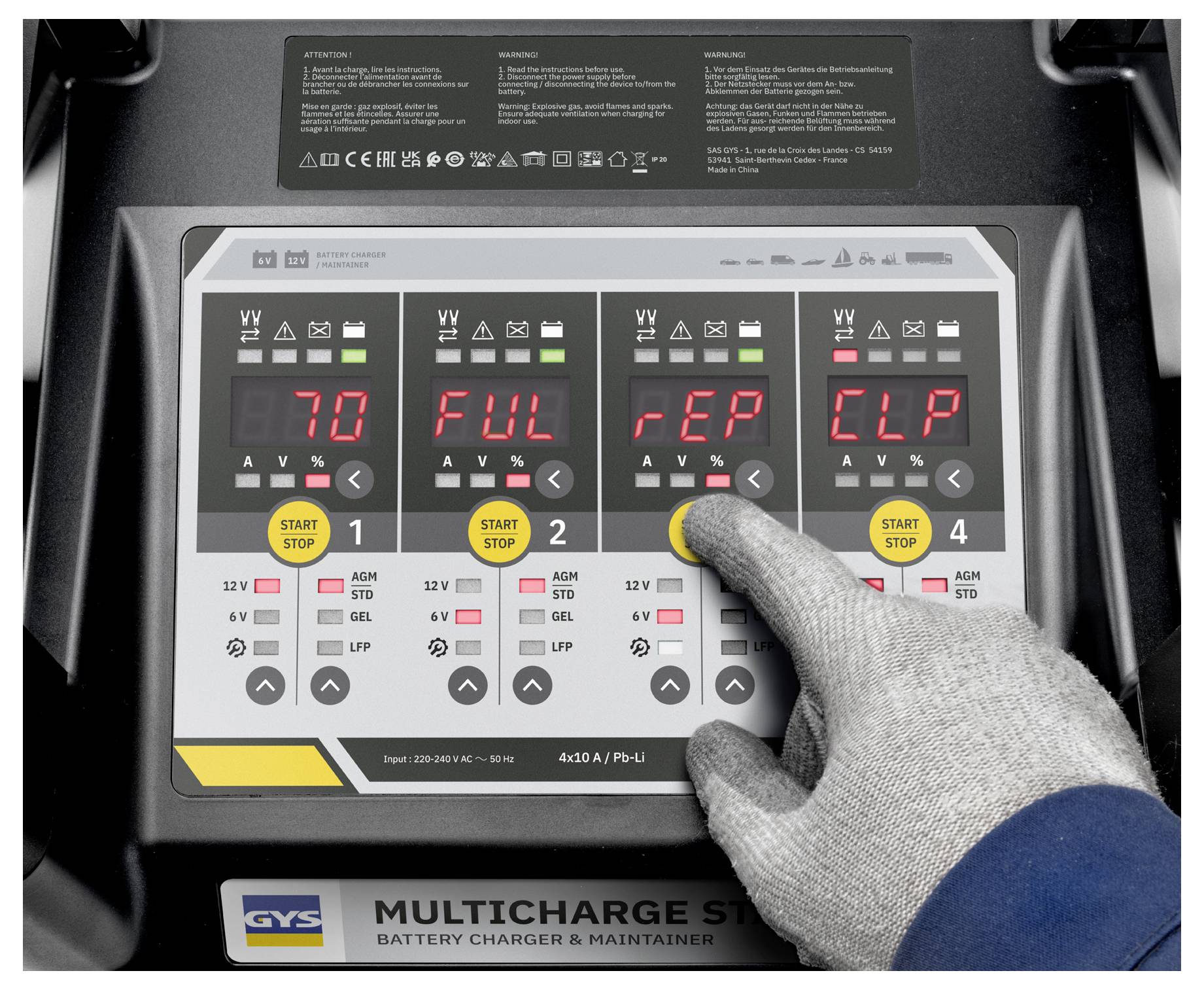 Eine behandschuhte Hand drückt einen Knopf auf dem Display eines Batterieladegeräts. Der Bildschirm zeigt Einstellungen mit Zahlen und Abkürzungen; die erste lautet „70