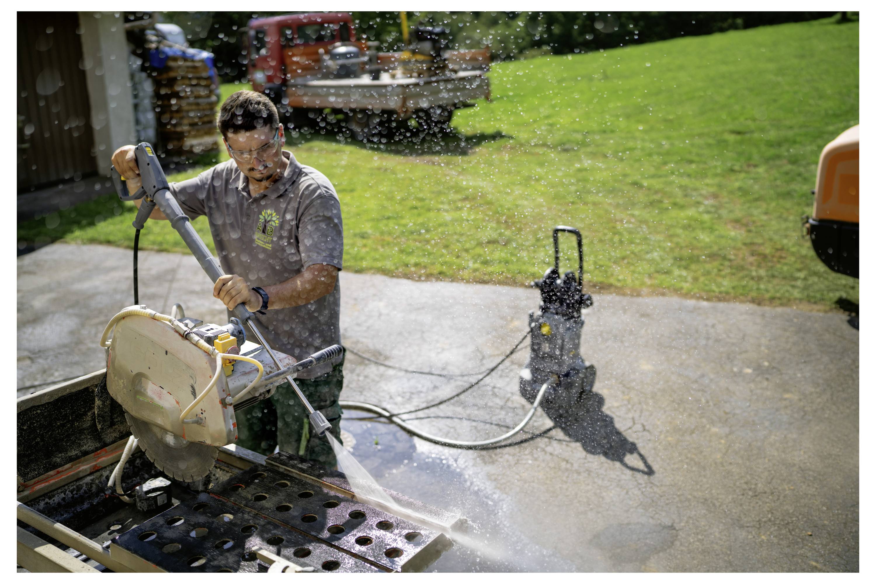 Eine Person benutzt eine Elektrosäge, um Material auf einer Außenfläche zu schneiden; Wasser spritzt aus der Säge und hält den Bereich nass.