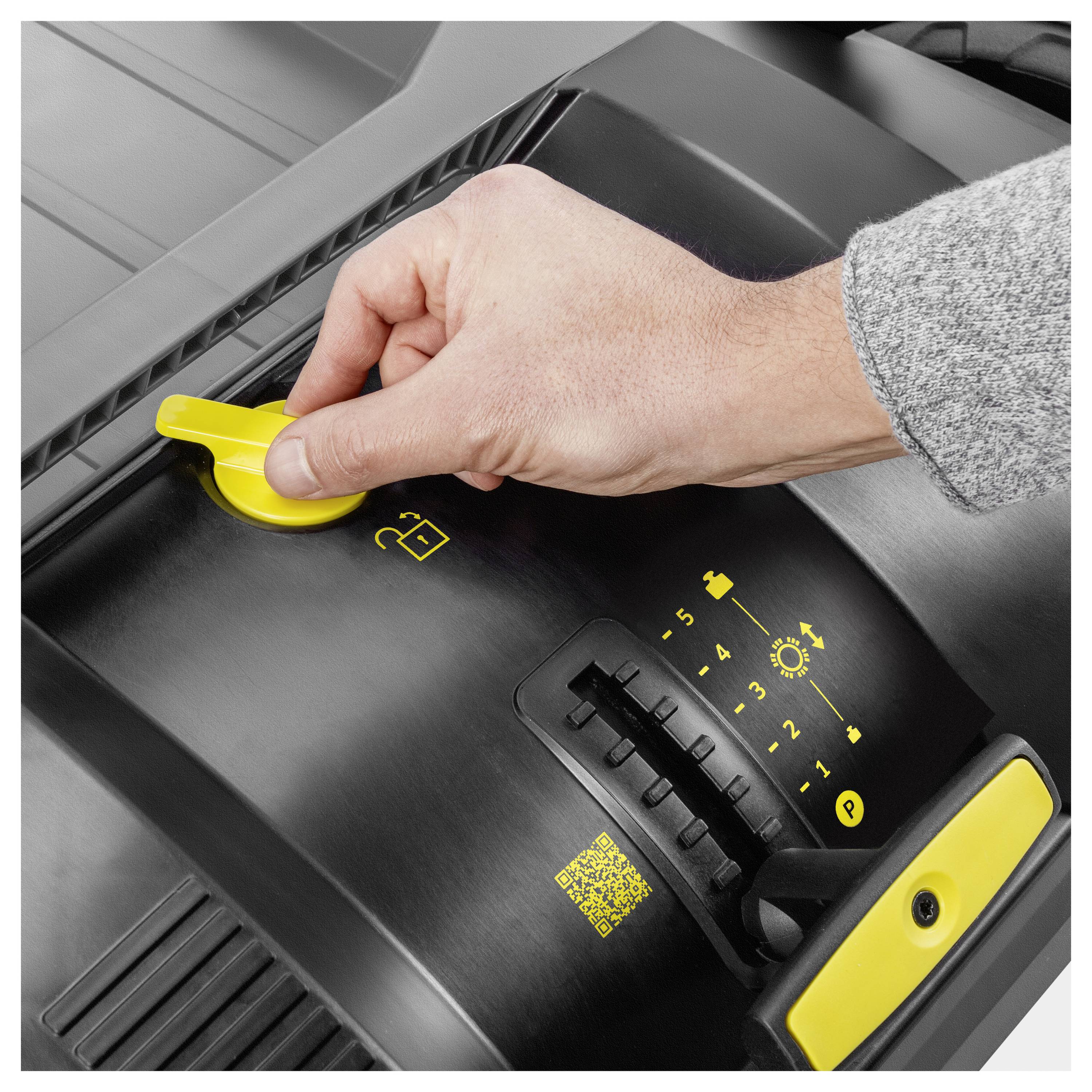 Die Hand einer Person stellt einen gelben Hebel an einer Maschine mit einem nummerierten Zifferblatt und kleinen Symbolen ein, was auf anpassbare Einstellungen hinweist.