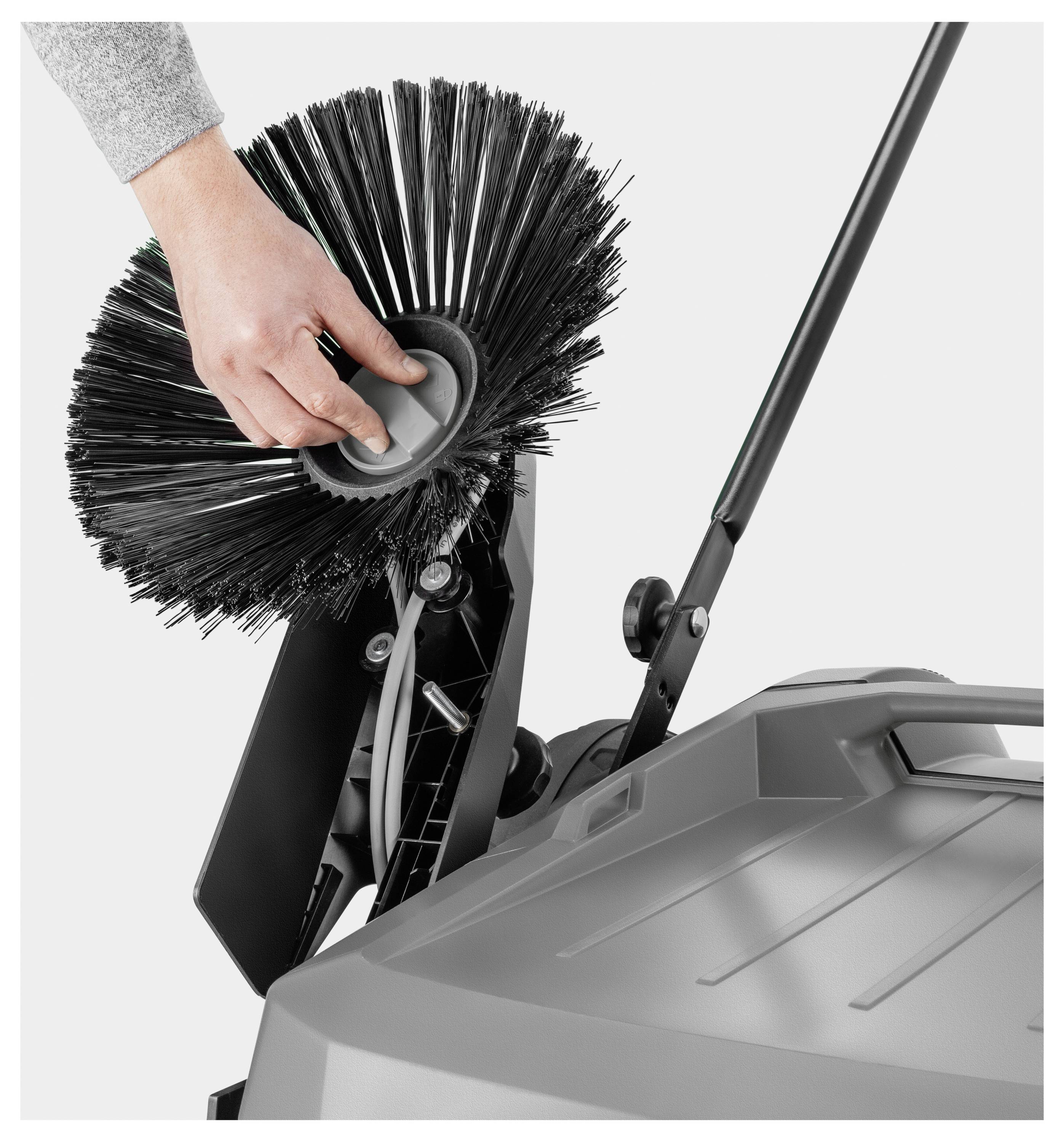 Hand, die die Bürste einer grauen Reinigungsmaschine mit schwarzem Griff einstellt, zeigt eine Nahaufnahme des Bürstenmechanismus.