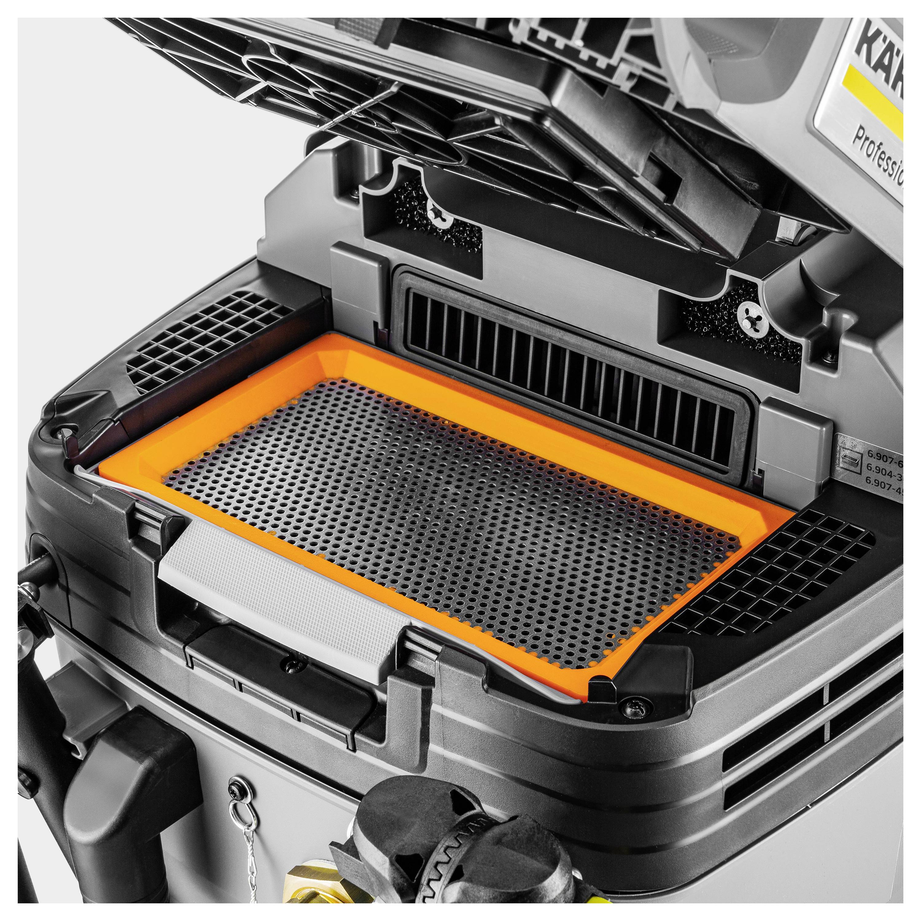 Eine Nahaufnahme eines grau-orangefarbenen Luftfilters in einer mechanischen Vorrichtung, die das rechteckige Filtergehäuse mit Gittermuster und offener Abdeckung zeigt.